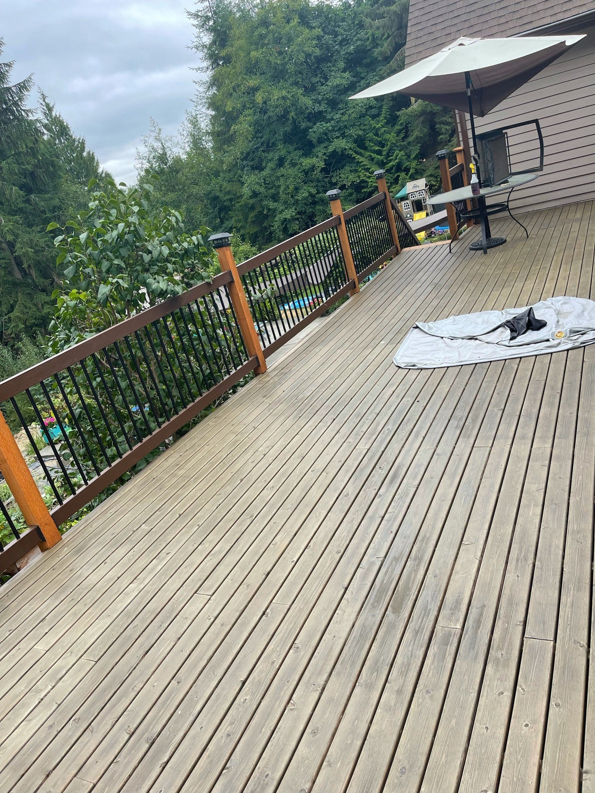 Wooden deck with black metal railing, umbrella, and trees in background.