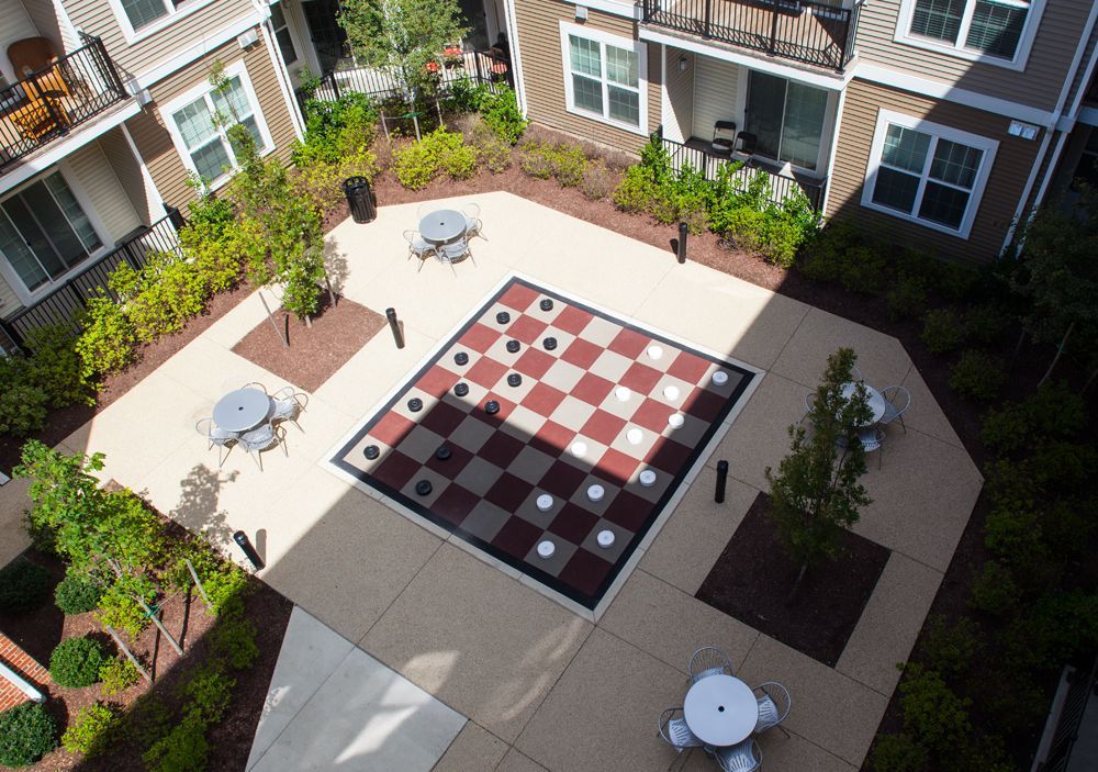 Courtyard with a giant checkerboard game, tables, and surrounding apartment buildings at Verde at Howard Square West Apartments in Elkridge, MD.