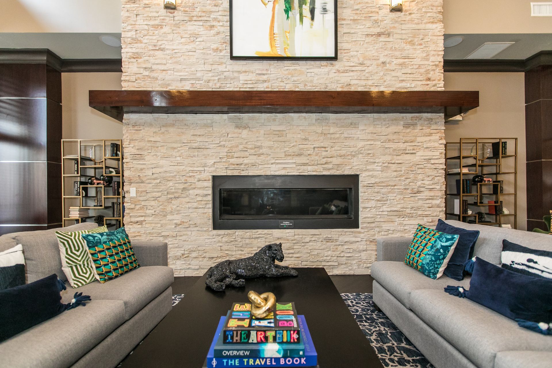 Modern living room with stone fireplace, two gray sofas, and a colorful coffee table book stack at Verde at Howard Square West Apartments in Elkridge, MD.