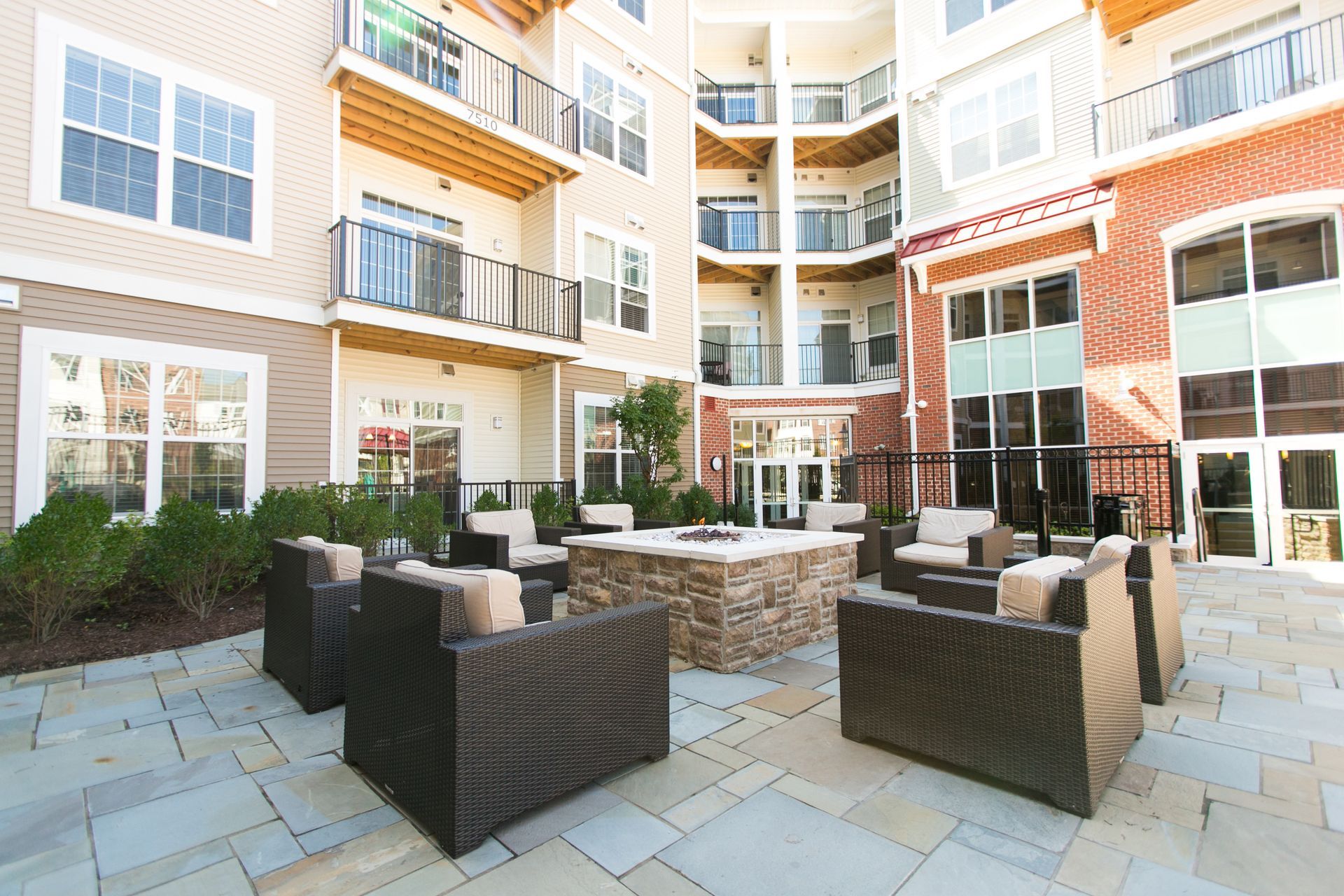 Courtyard patio with wicker seating and tables in a modern apartment building courtyard at Verde at Howard Square West Apartments in Elkridge, MD.