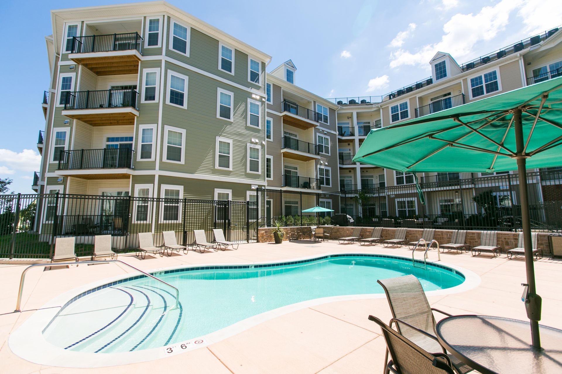 Apartment complex pool with turquoise water, lounge chairs, and a green shade canopy under a blue sky at Verde at Howard Square West Apartments in Elkridge, MD