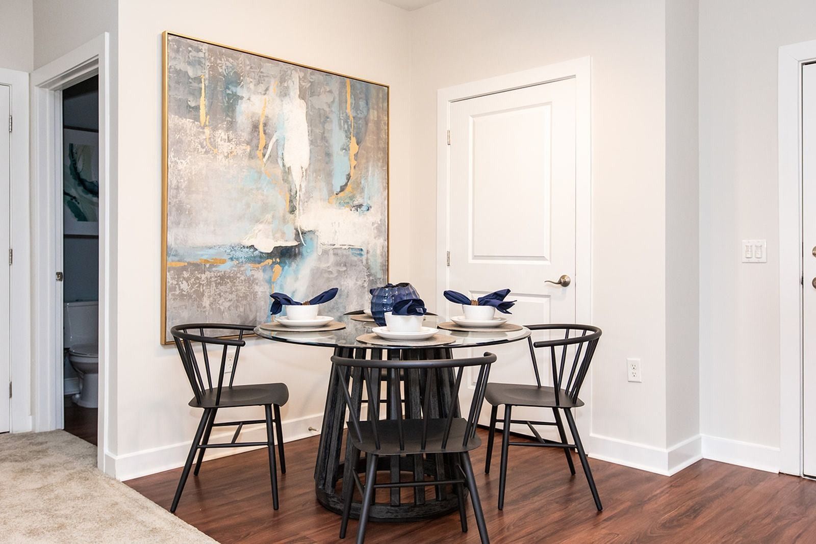 Modern dining nook with black chairs, white table, and abstract wall art in a bright room at Verde at Howard Square West Apartments in Elkridge, MD.