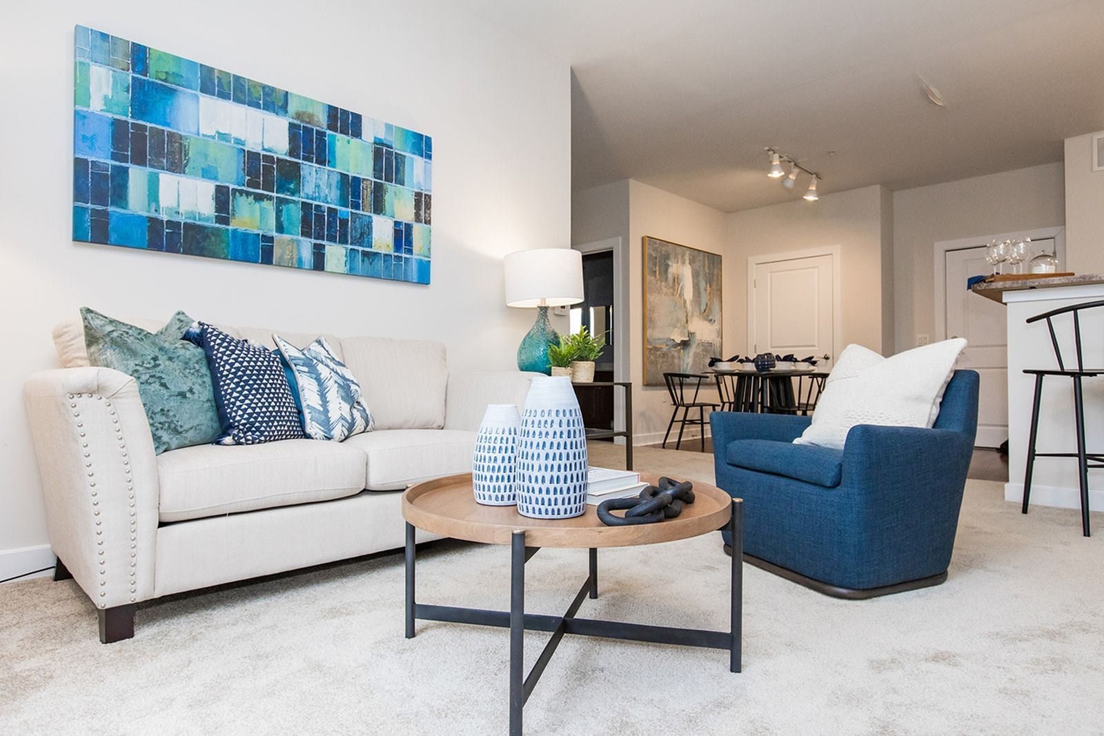 Bright modern living room with cream sofa, blue chair, abstract wall art, and coffee table at Verde at Howard Square West Apartments in Elkridge, MD.