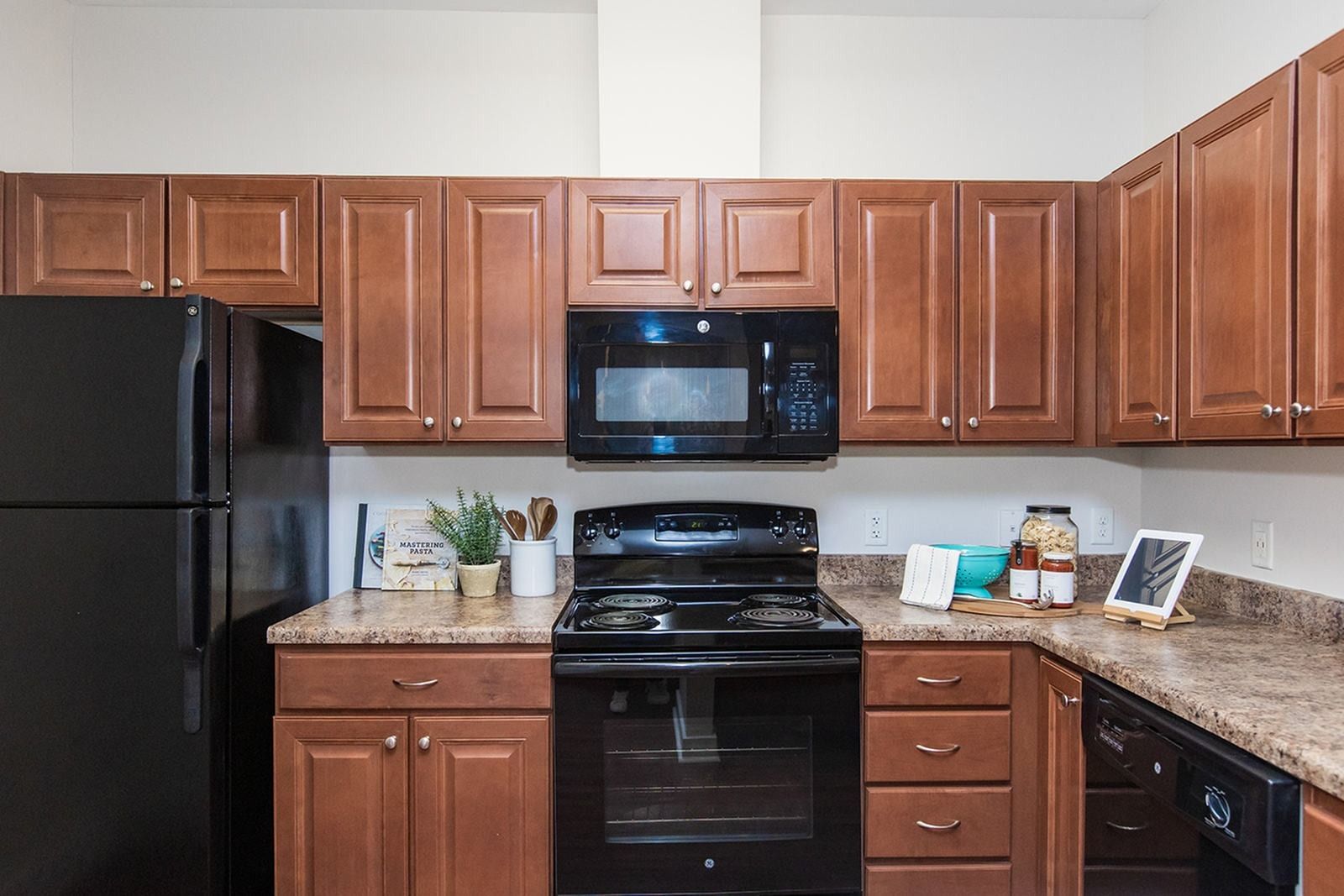 Modern kitchen with black appliances, brown cabinets, and granite countertops at Verde at Howard Square West Apartments in Elkridge, MD.