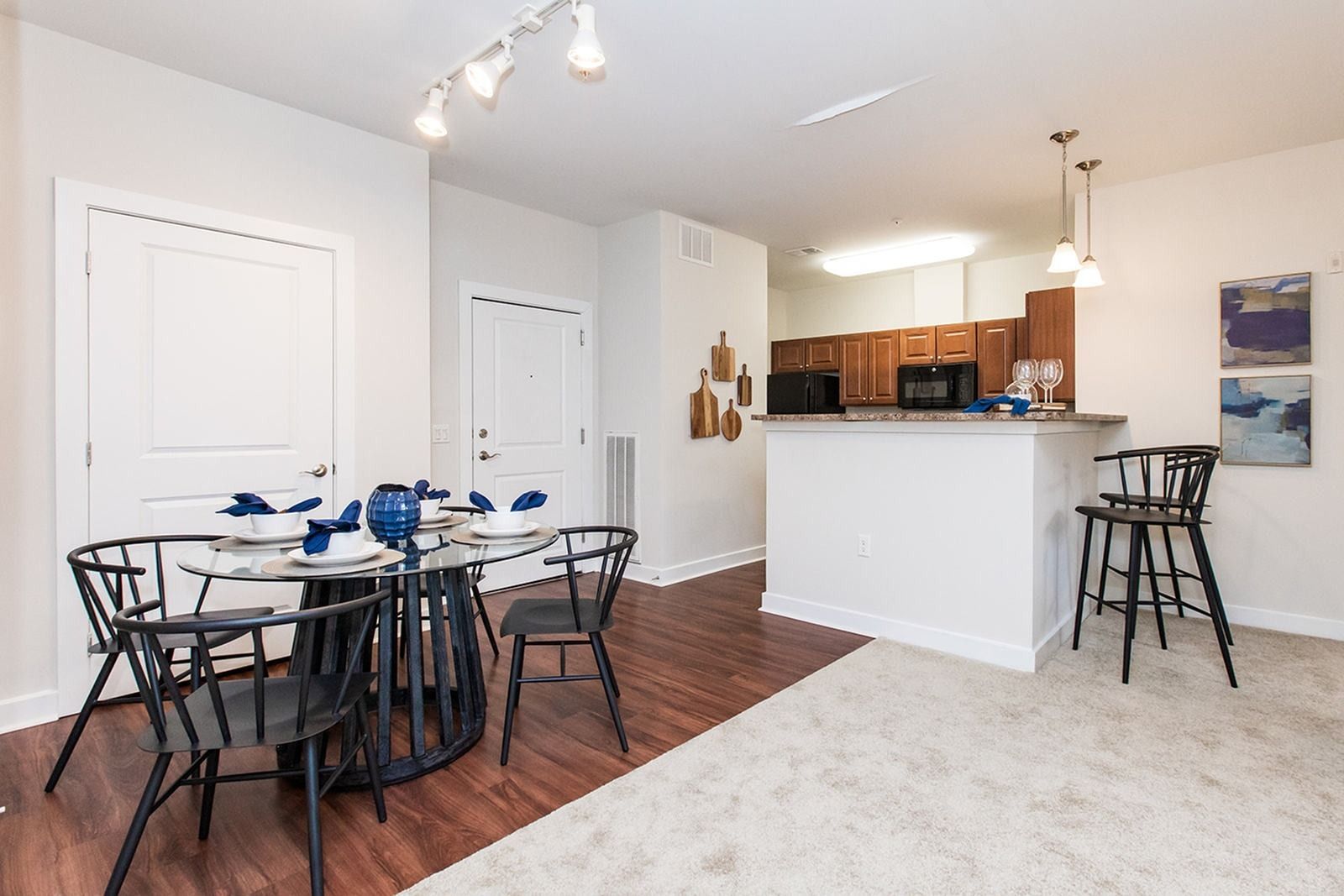 Open-plan dining and kitchen area with a black table, barstools, and wood floors at Verde at Howard Square West Apartments in Elkridge, MD.