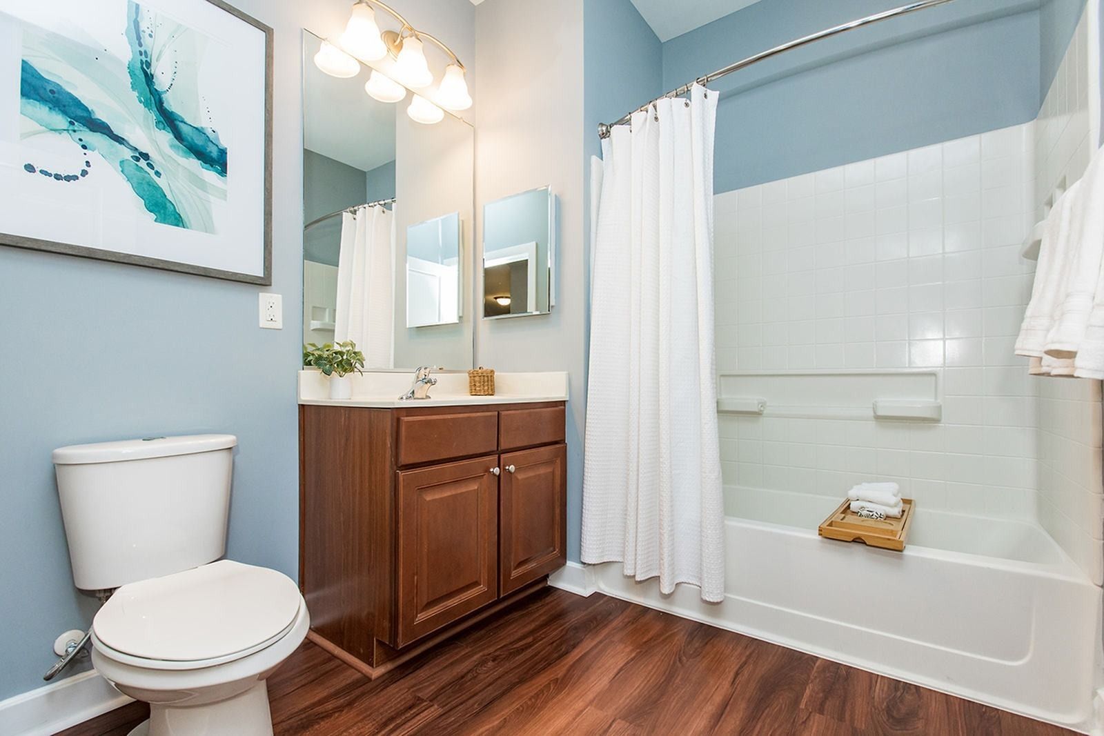 Bright bathroom with white tub and shower curtain, wood vanity, toilet, and teal walls at Verde at Howard Square West Apartments in Elkridge, MD.