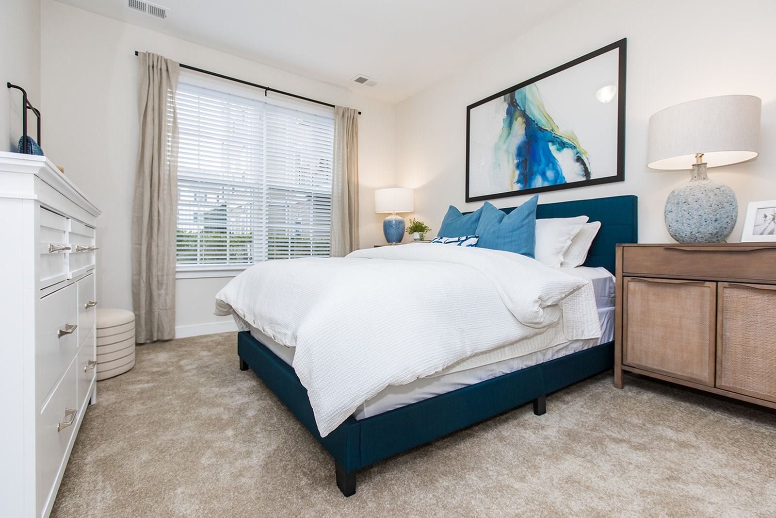 Bedroom with carpeted flooring, large window, and blue bed frame at Verde at Howard Square West Apartments in Elkridge, MD.