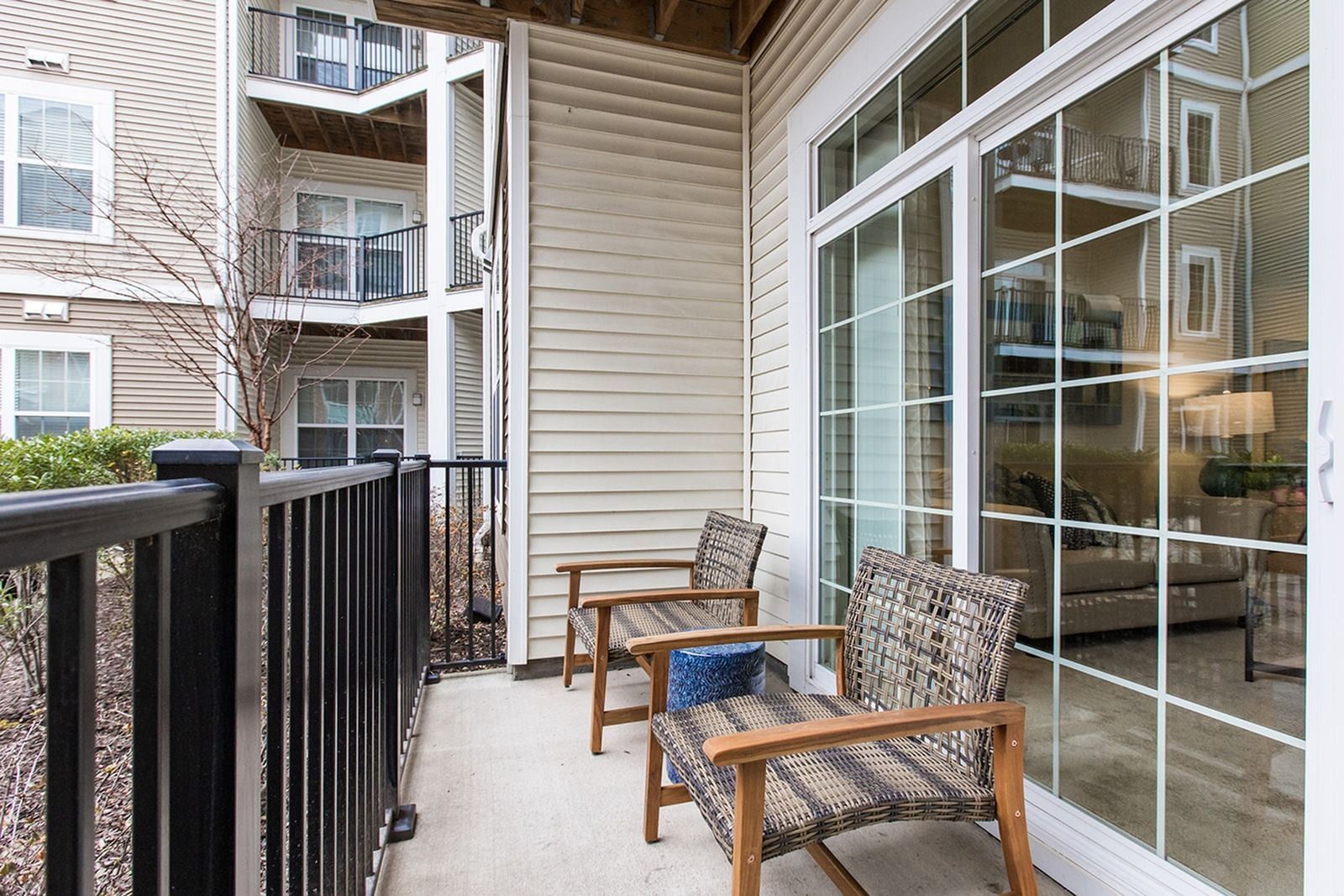 Apartment balcony with two chairs, black railing, and sliding glass doors beside a neighboring building at Verde at Howard Square West Apartments in Elkridge, MD.