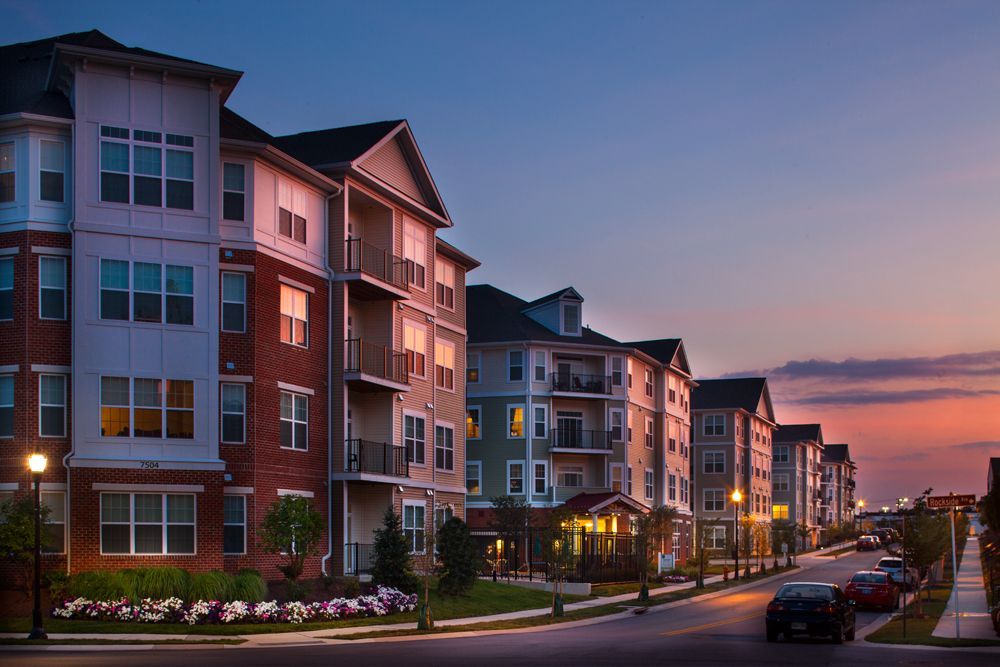 Apartment buildings on a sunset-lit street with parked cars and flower beds at Verde at Howard Square West Apartments in Elkridge, MD.