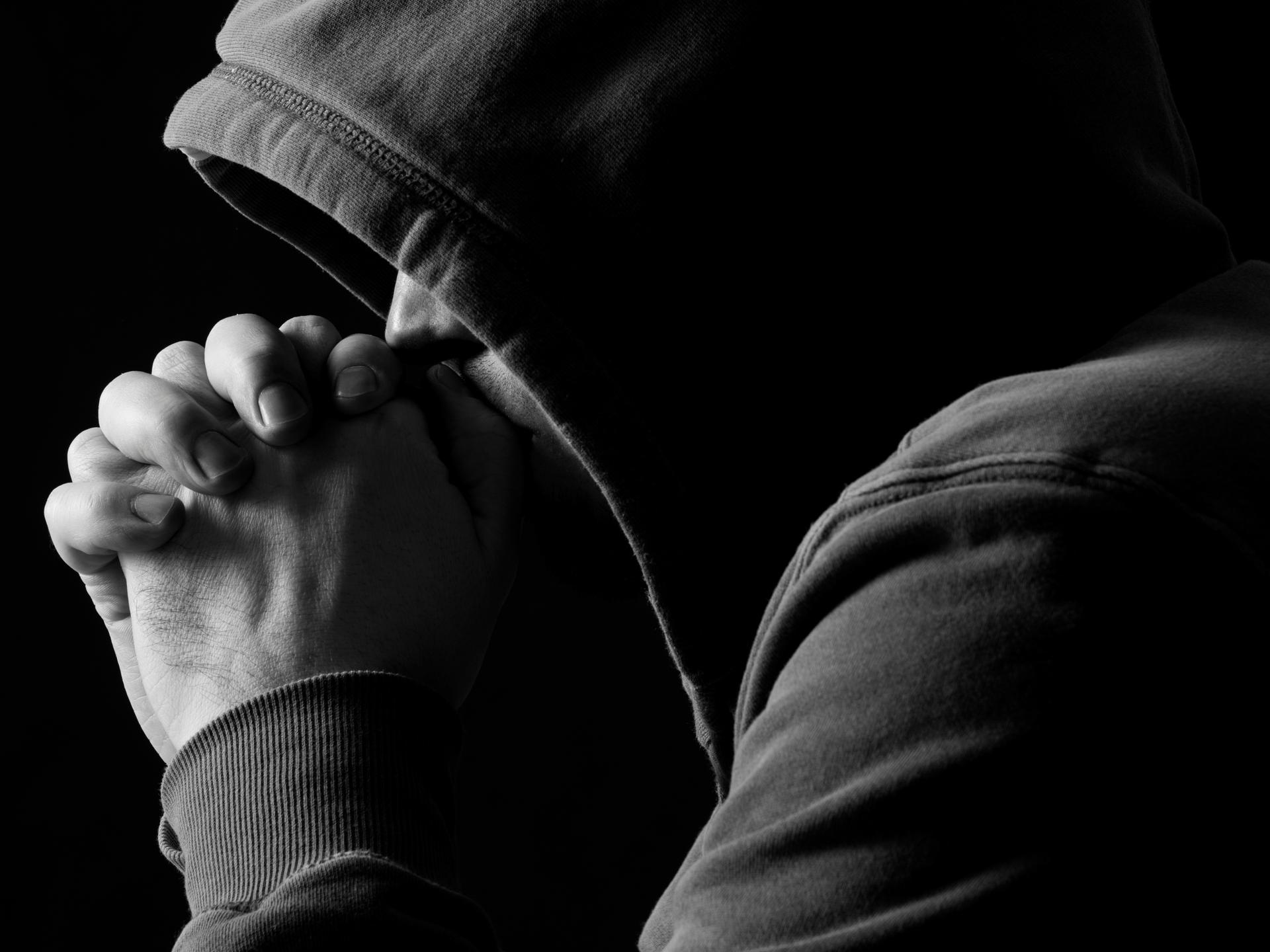 Person in hooded sweatshirt with clasped hands, in prayer or contemplation, in monochrome.