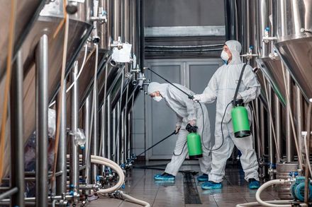 Two men in protective suits are cleaning a factory.