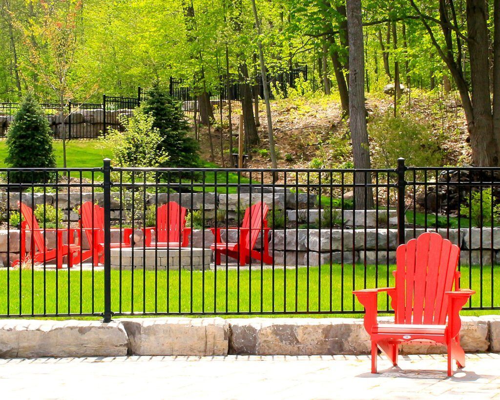 A red chair is sitting in front of a black fence.