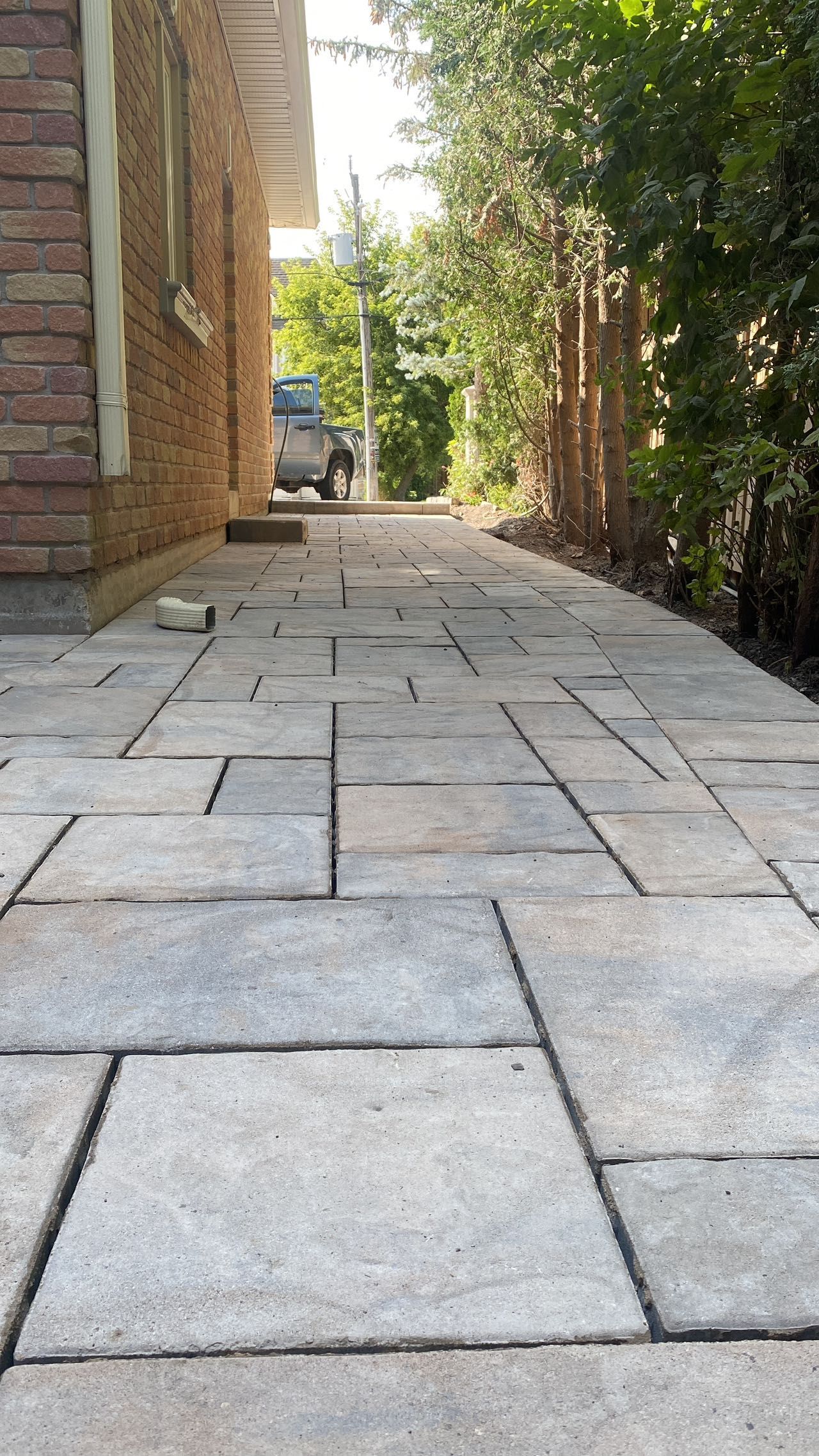A brick walkway leading to a brick house surrounded by trees.