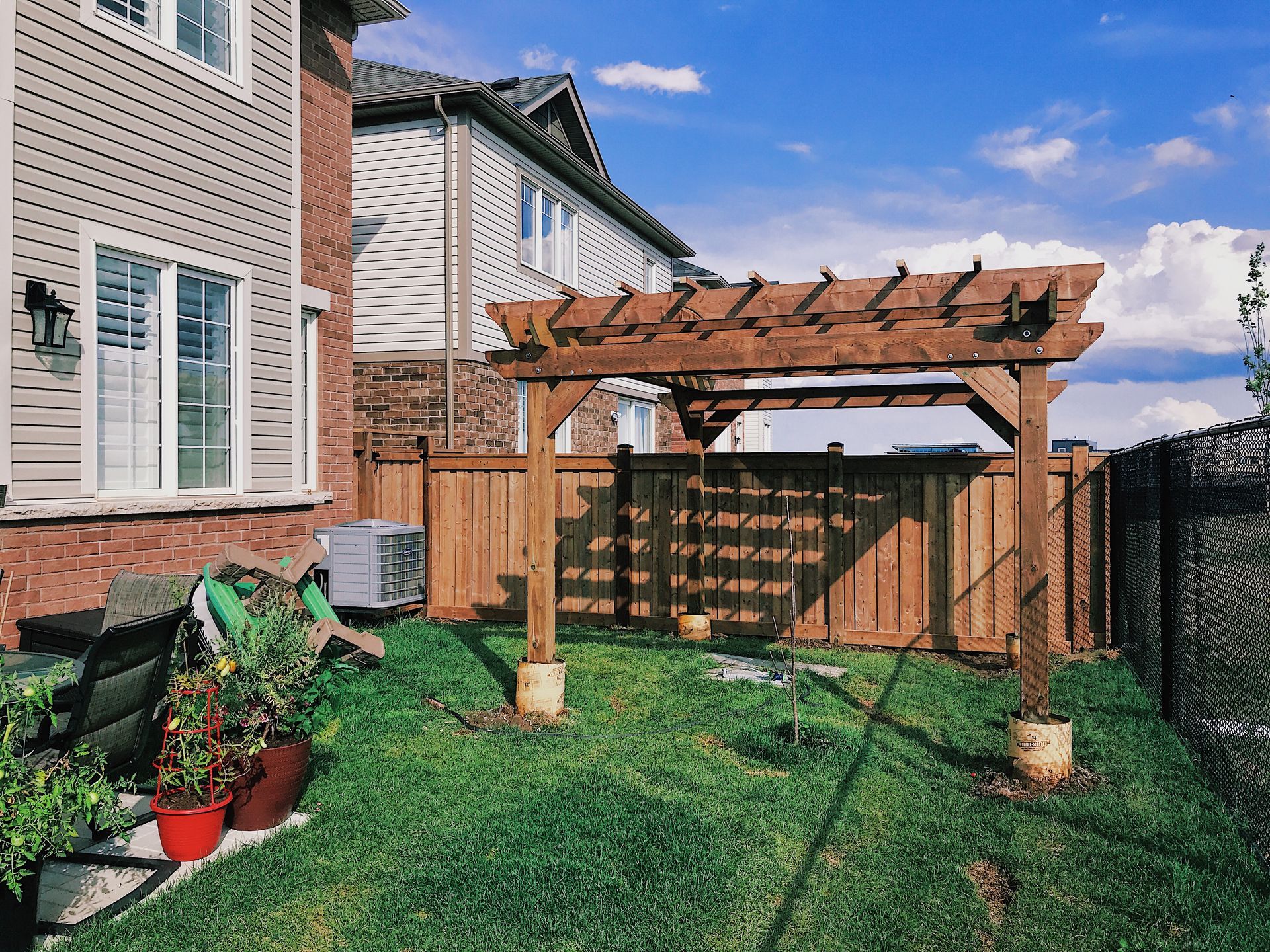 Backyard with wooden pergola, wooden fence, green grass, and residential houses on a sunny day.