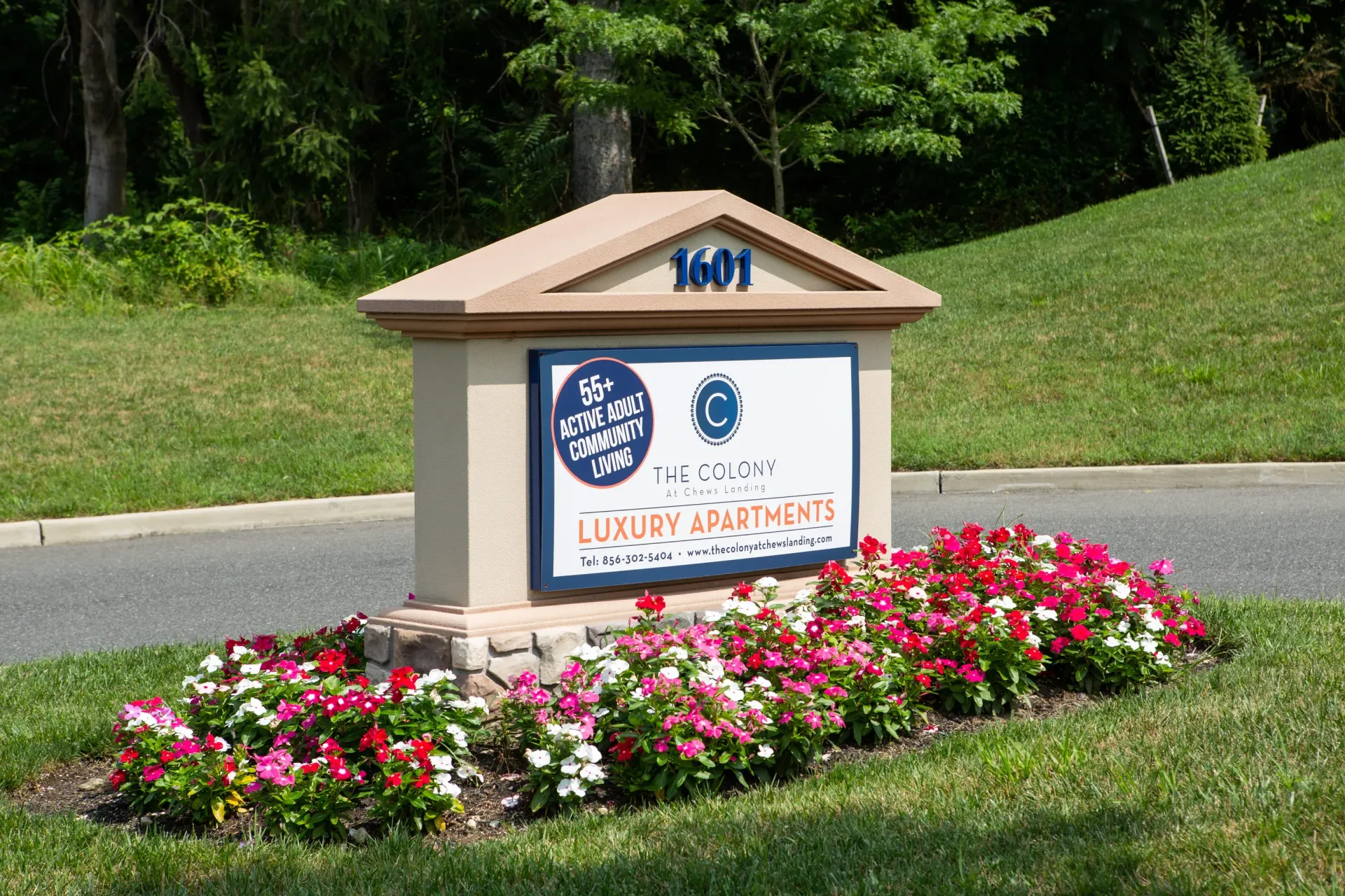 Entrance monument sign for The Colony Luxury Apartments with a colorful flower bed in front.