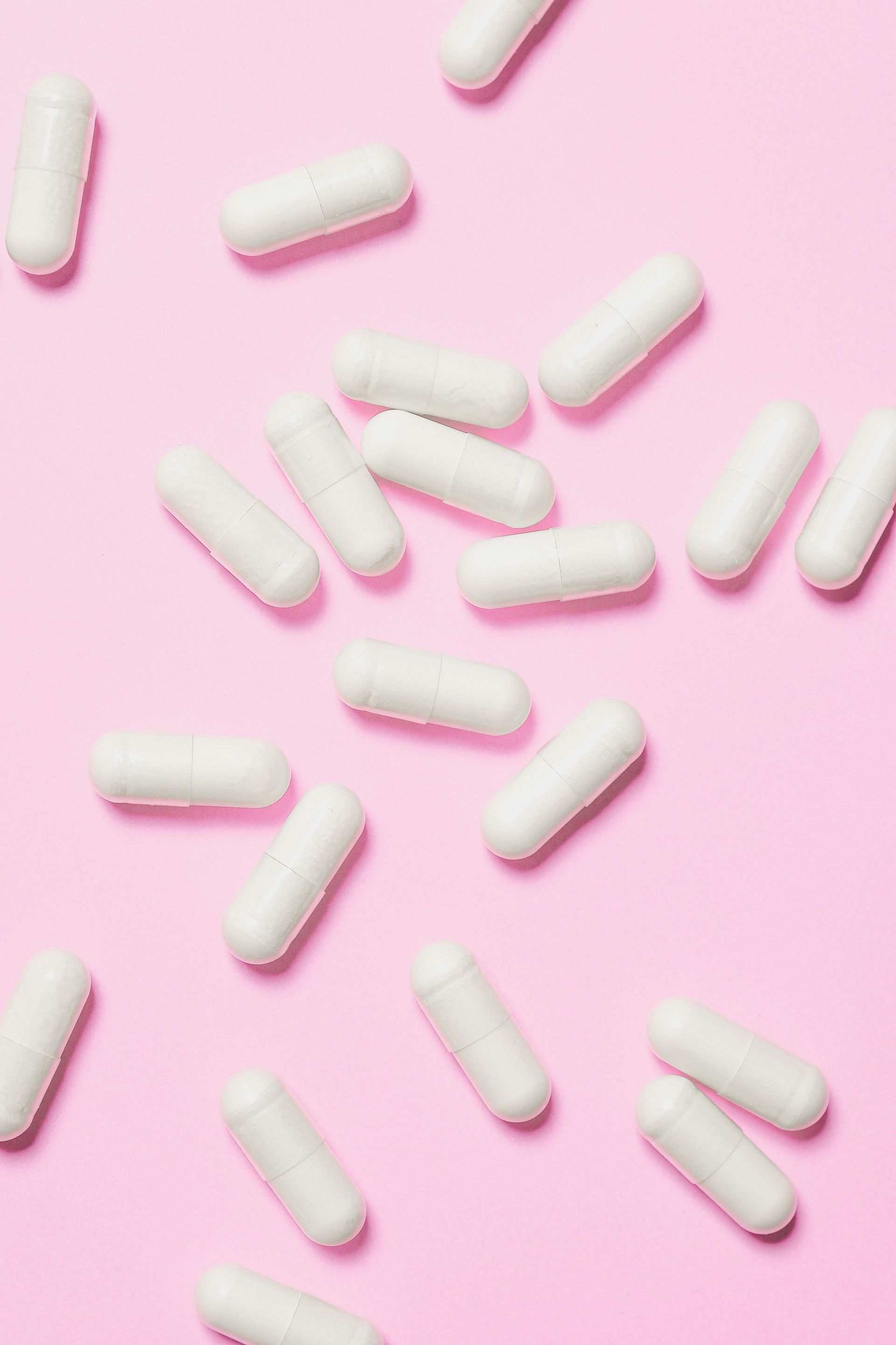 A bunch of white pills on a pink background.