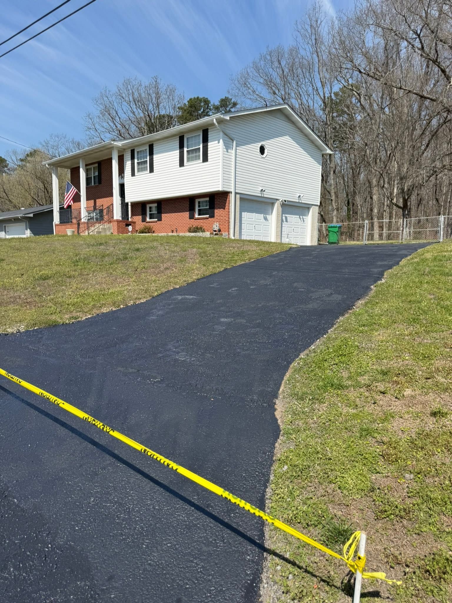 Asphalt driveway after repair, in front of a blue house with landscaping and green grass.