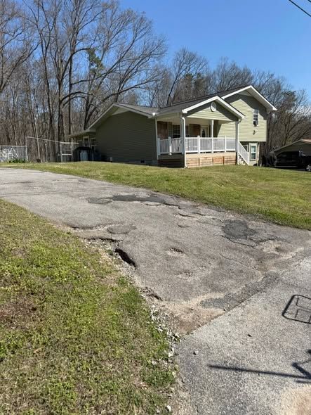 Asphalt driveway before sealing, a long hose on the ground, a shadow.