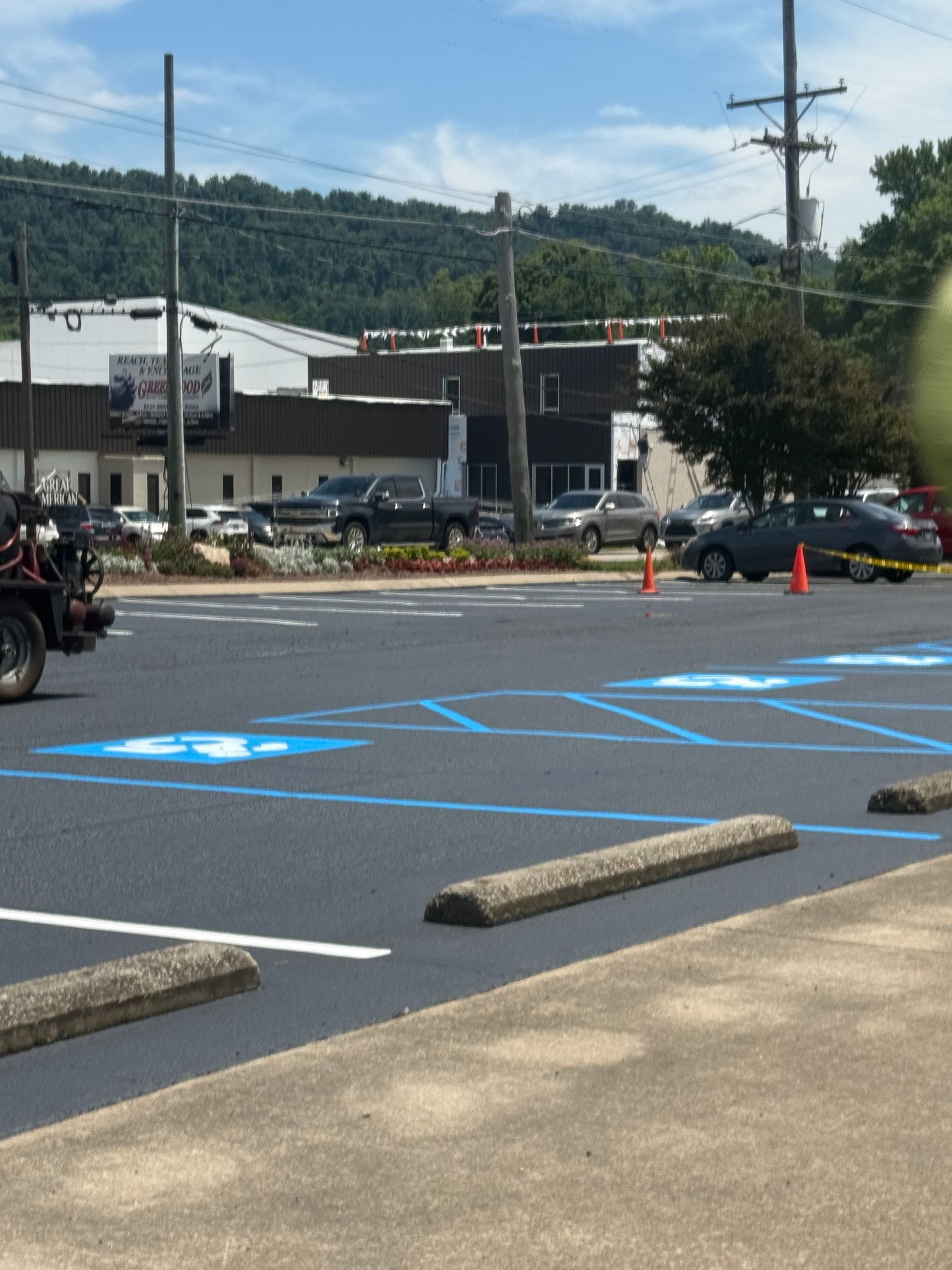 Asphalt parking lot with blue handicap space symbol and orange cones. White lines mark parking spaces.