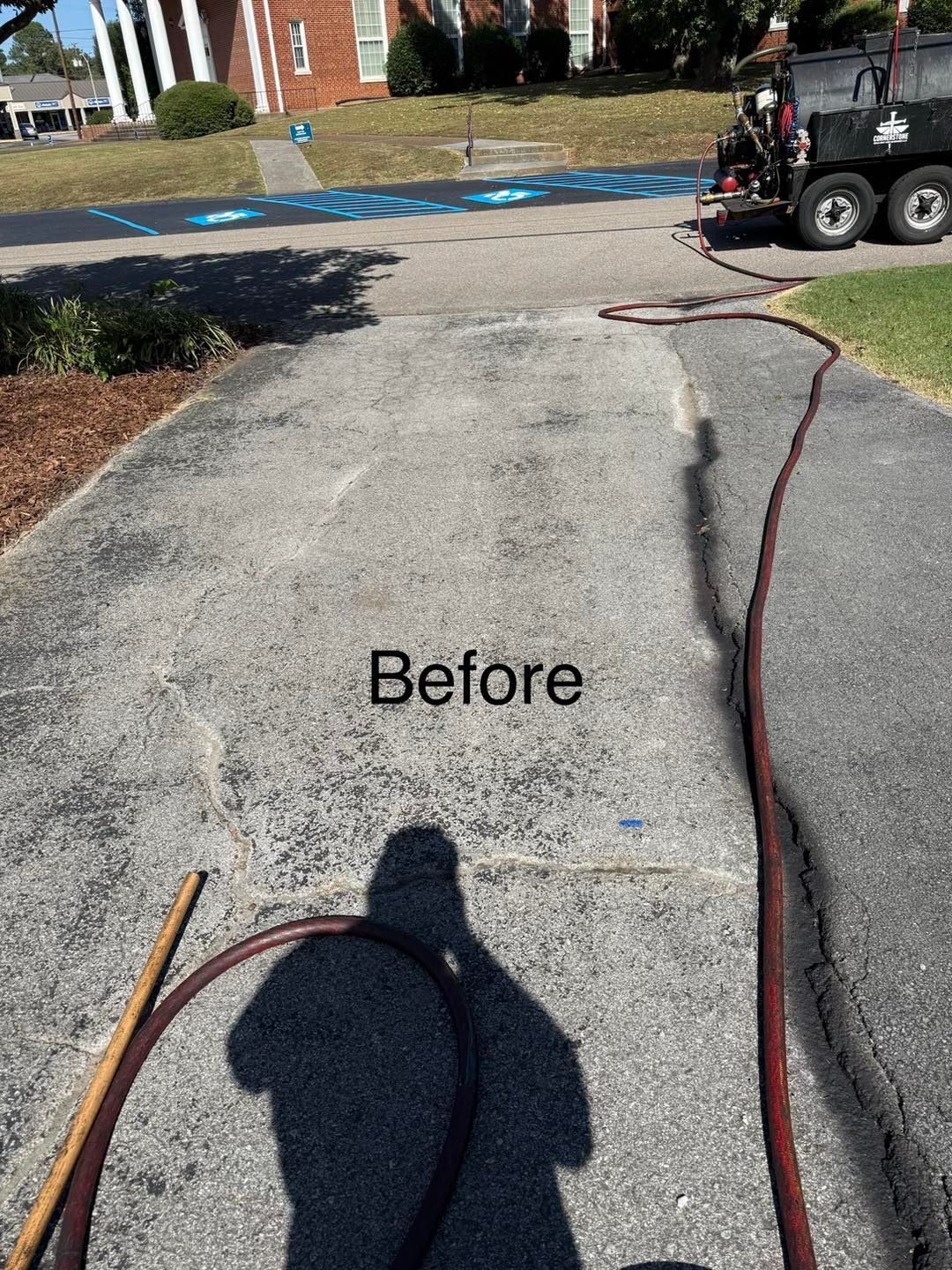 Asphalt driveway before sealing, a long hose on the ground, a shadow.