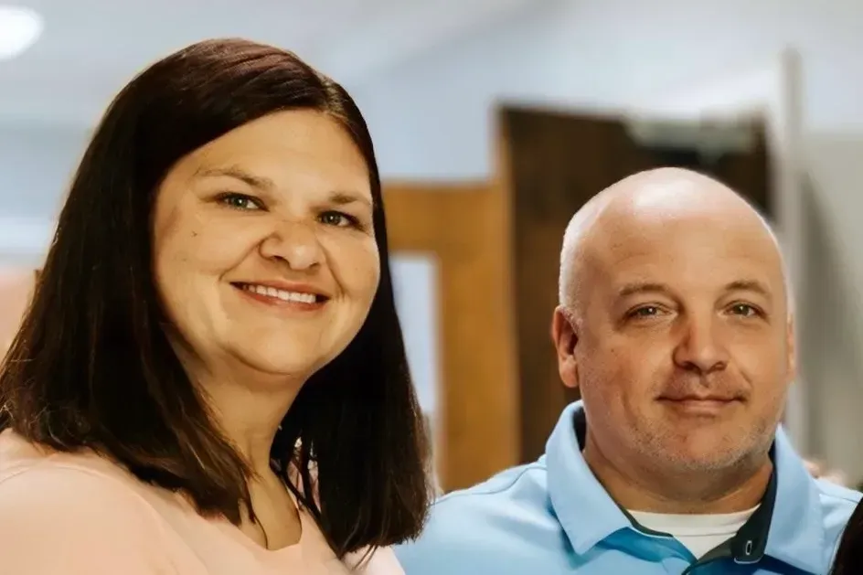 Woman in pink and man in blue polo shirt smiling indoors, close up.