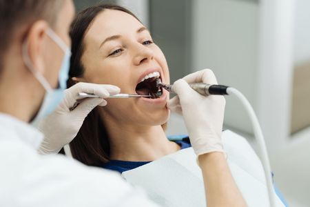 A dentist in a white coat and mask performs a dental procedure on a patient in a chair.