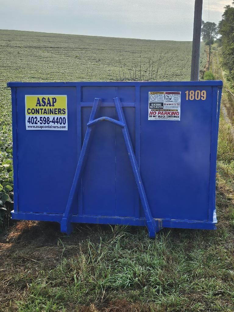 A blue dumpster rental is sitting in the middle of a grassy field.