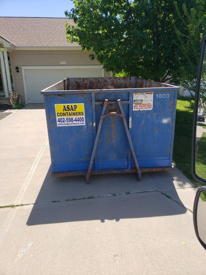 A blue dumpster is parked in front of a house in a driveway.