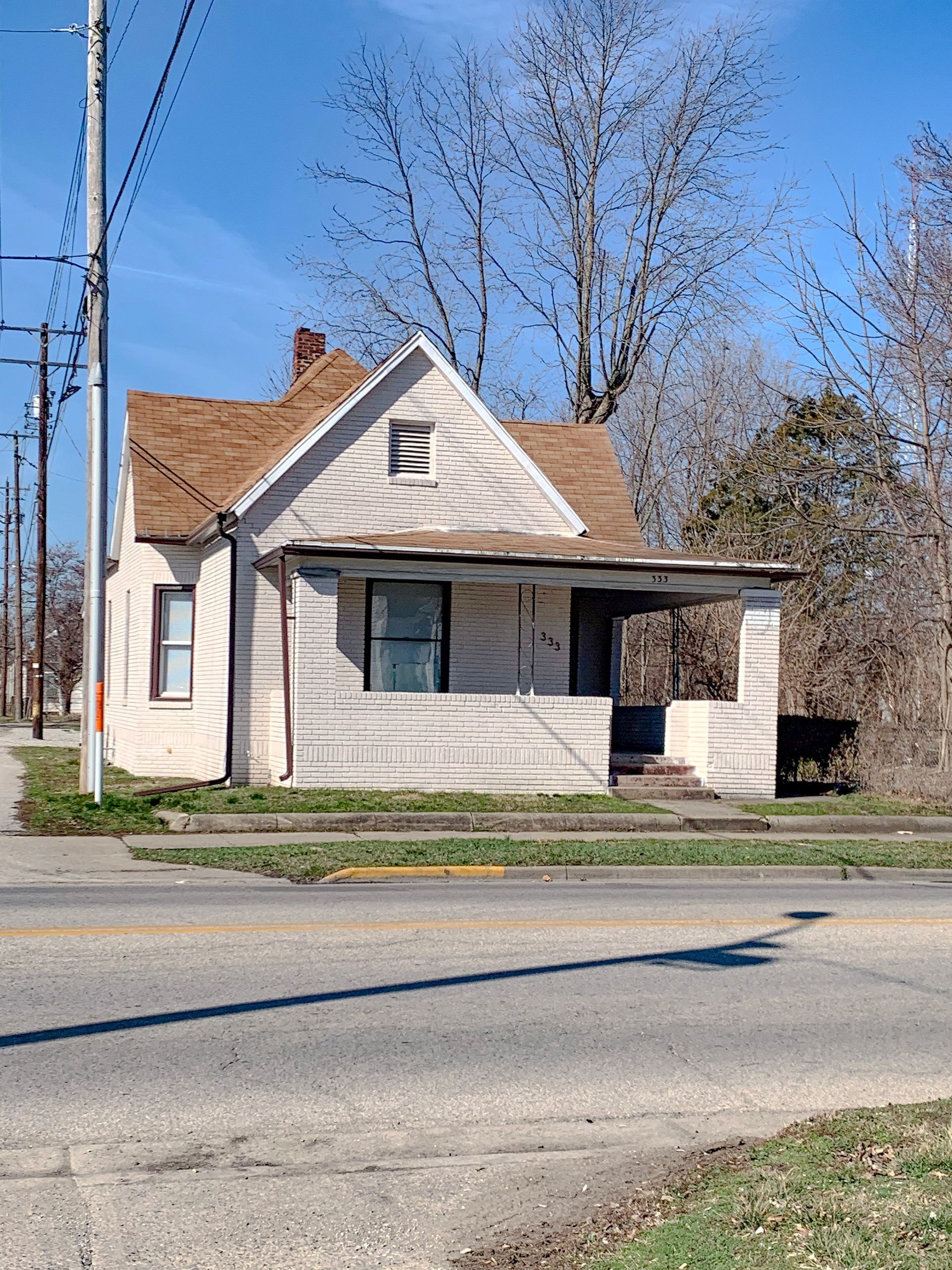 A small white house with a brown roof sits on the side of the road