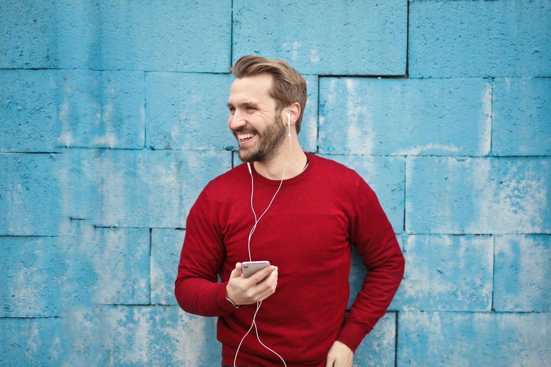 A man in a red sweater is listening to music on his phone