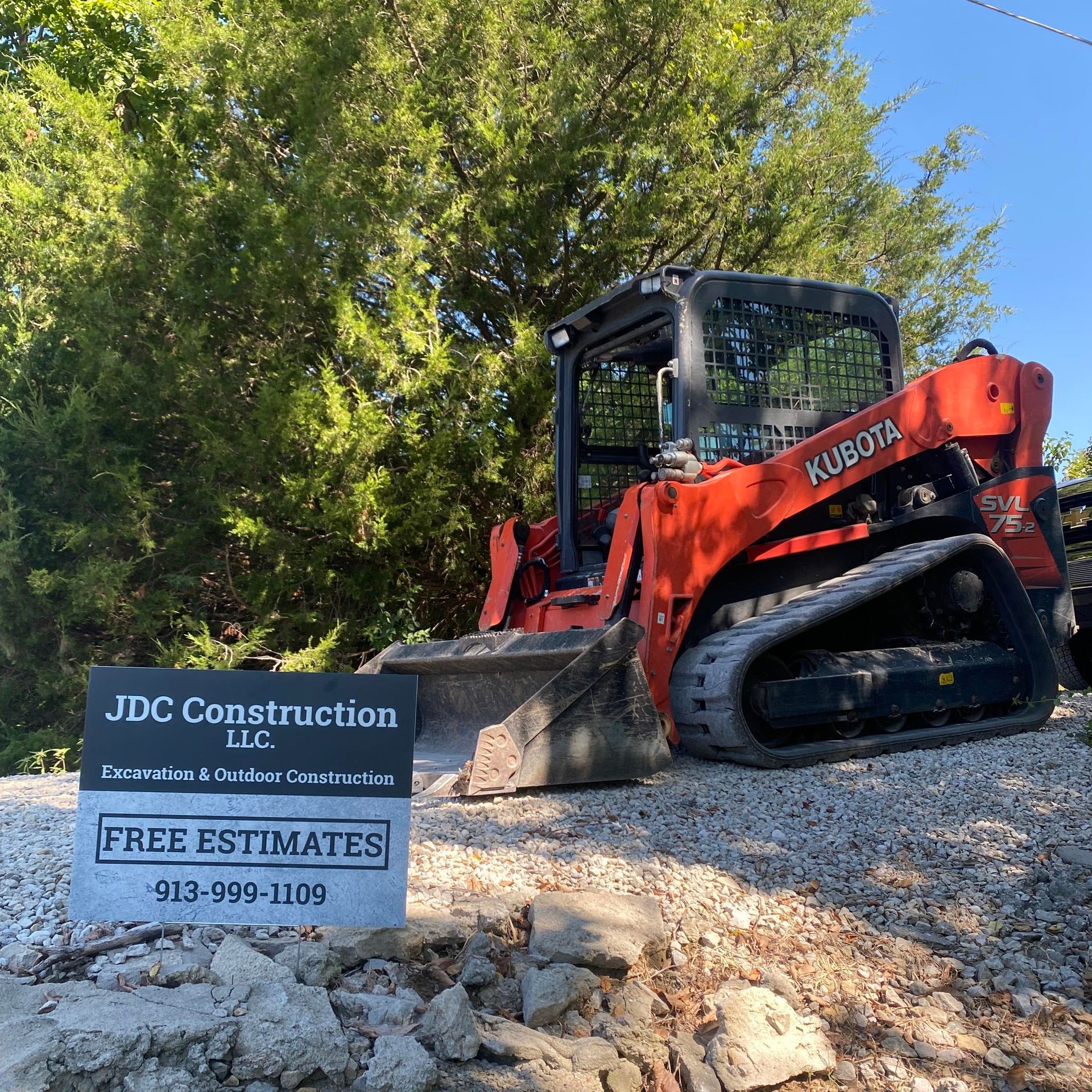 Orange Kubota skid steer beside a JDC Construction free estimates sign on a gravel driveway