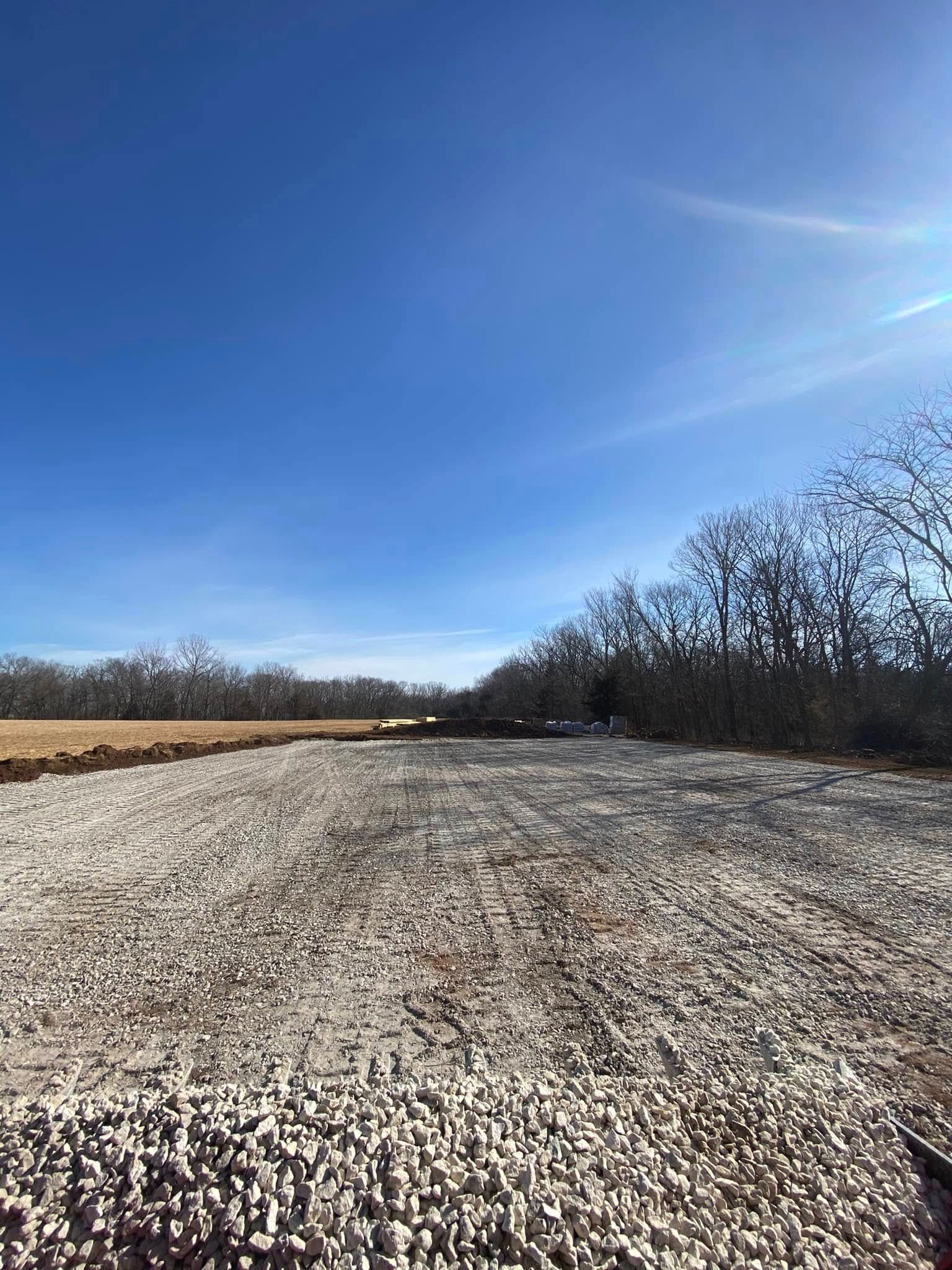 Gravel path beside a field under a bright blue sky with bare trees in the distance