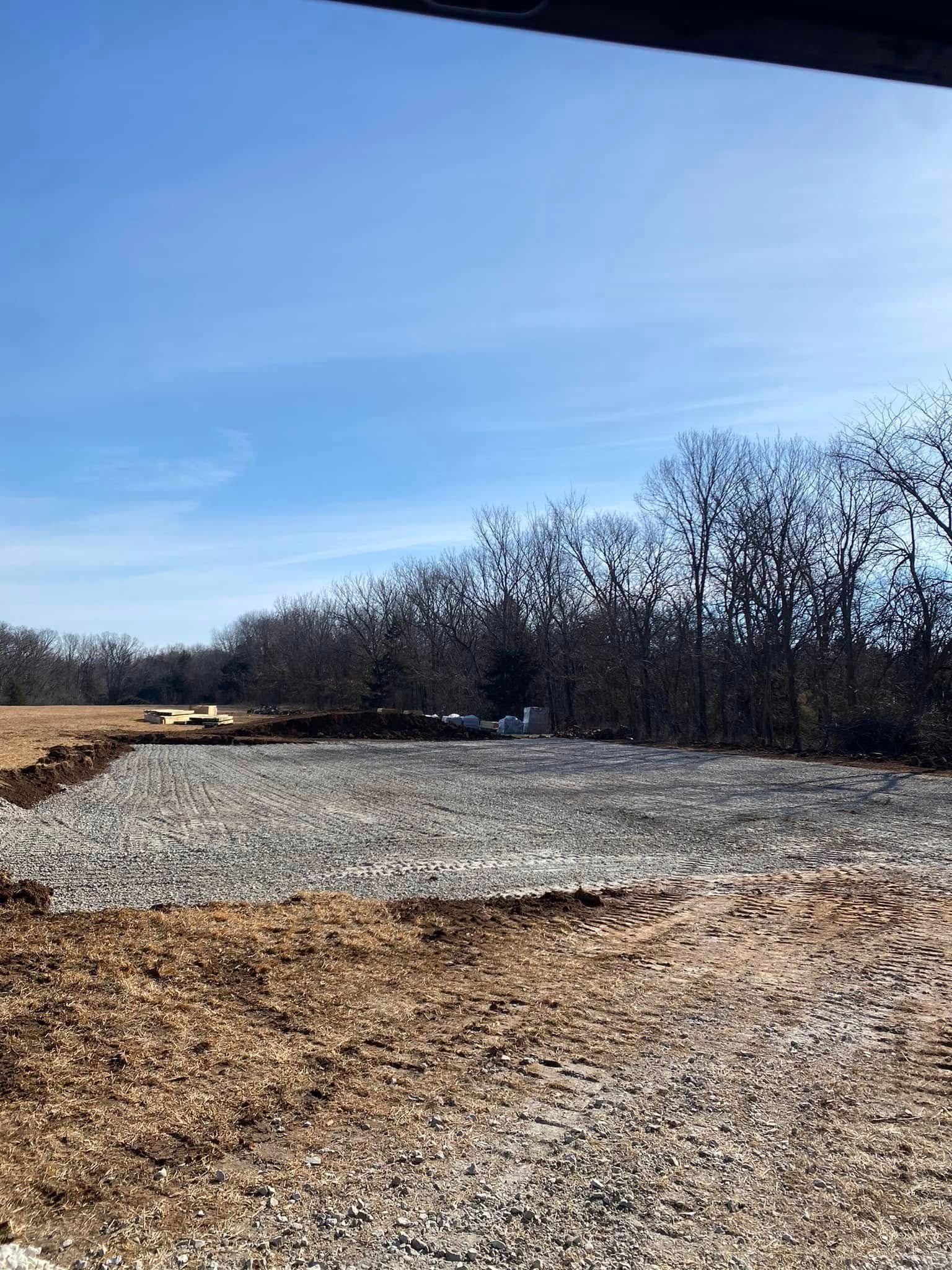 Snow-dusted gravel lot beside bare trees under a clear blue sky