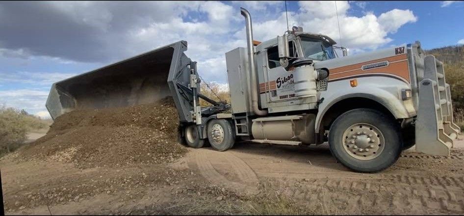 Dump truck unloading gravel at a construction site under a cloudy sky