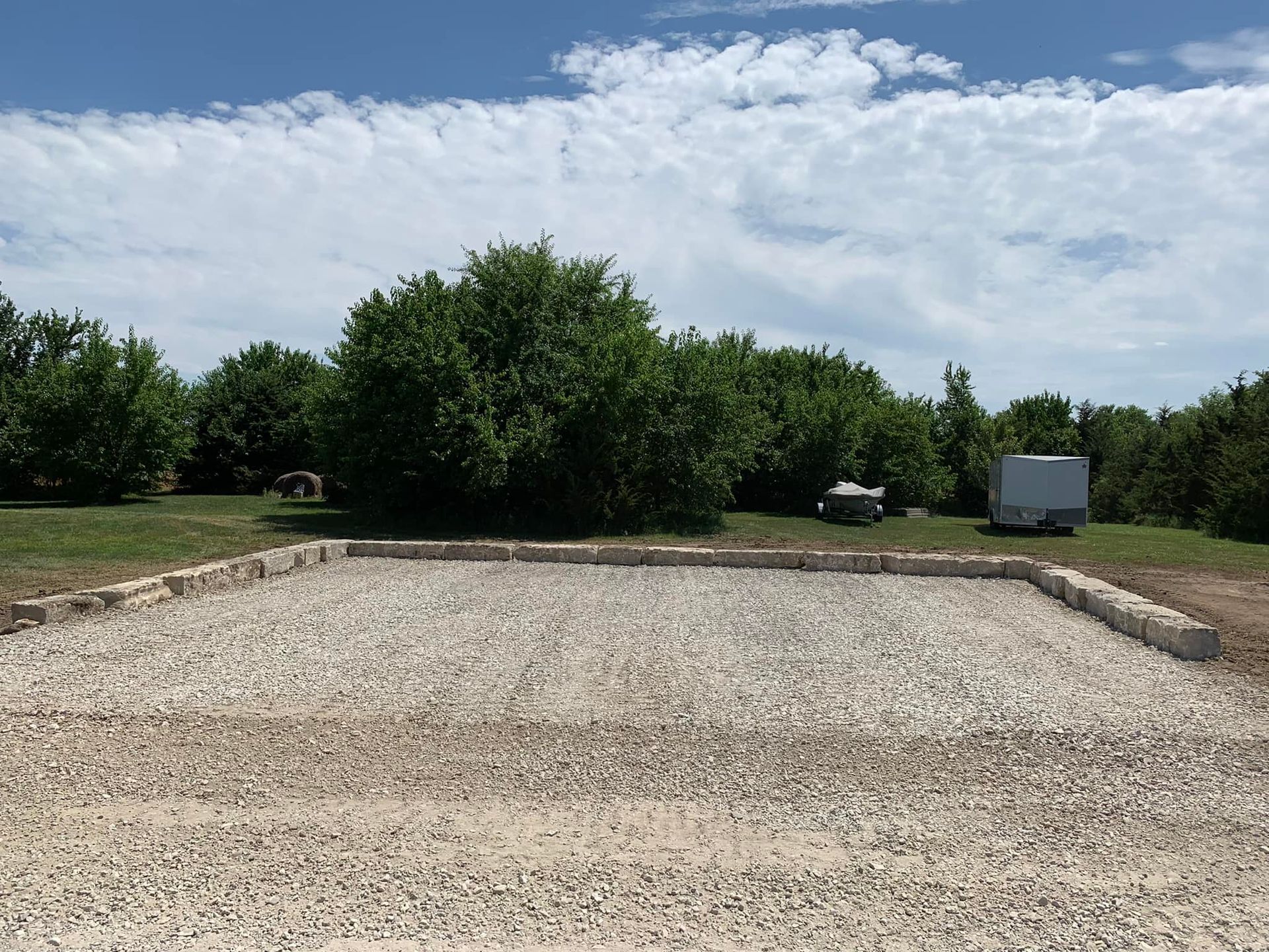 Gravel lot under construction with trees, blue sky, and a white truck in the background
