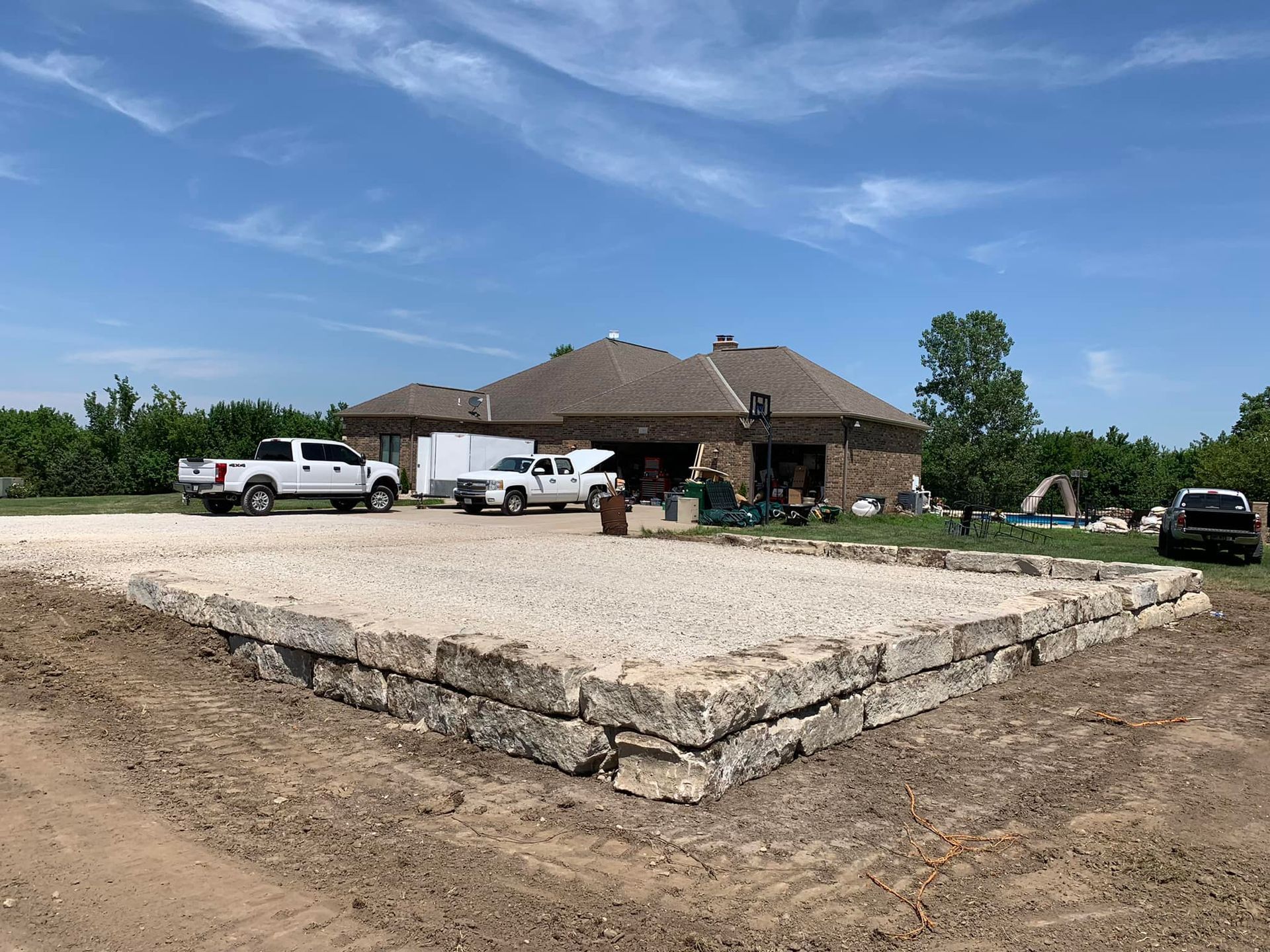Large stone foundation in front of a house under construction, with trucks and a clear blue sky