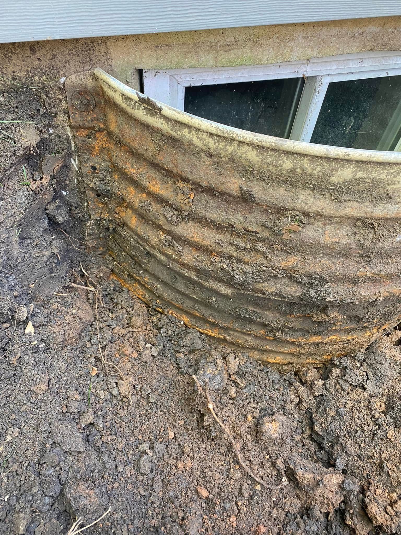 Rusty corrugated vent pipe protruding from a gravel-covered roof near a window opening
