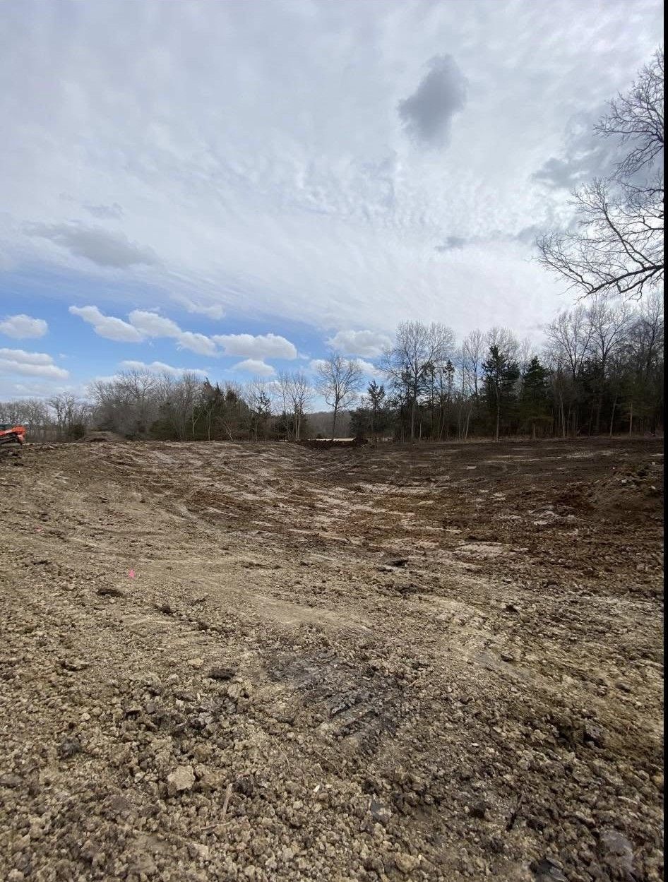 Barren dirt field under a cloudy sky with a tree line in the distance