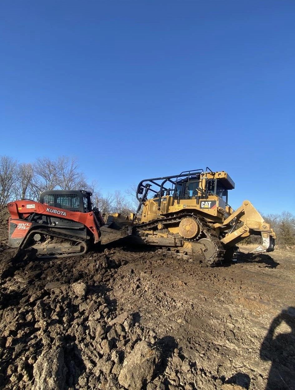 Two bulldozers on a muddy dirt mound under a clear blue sky.