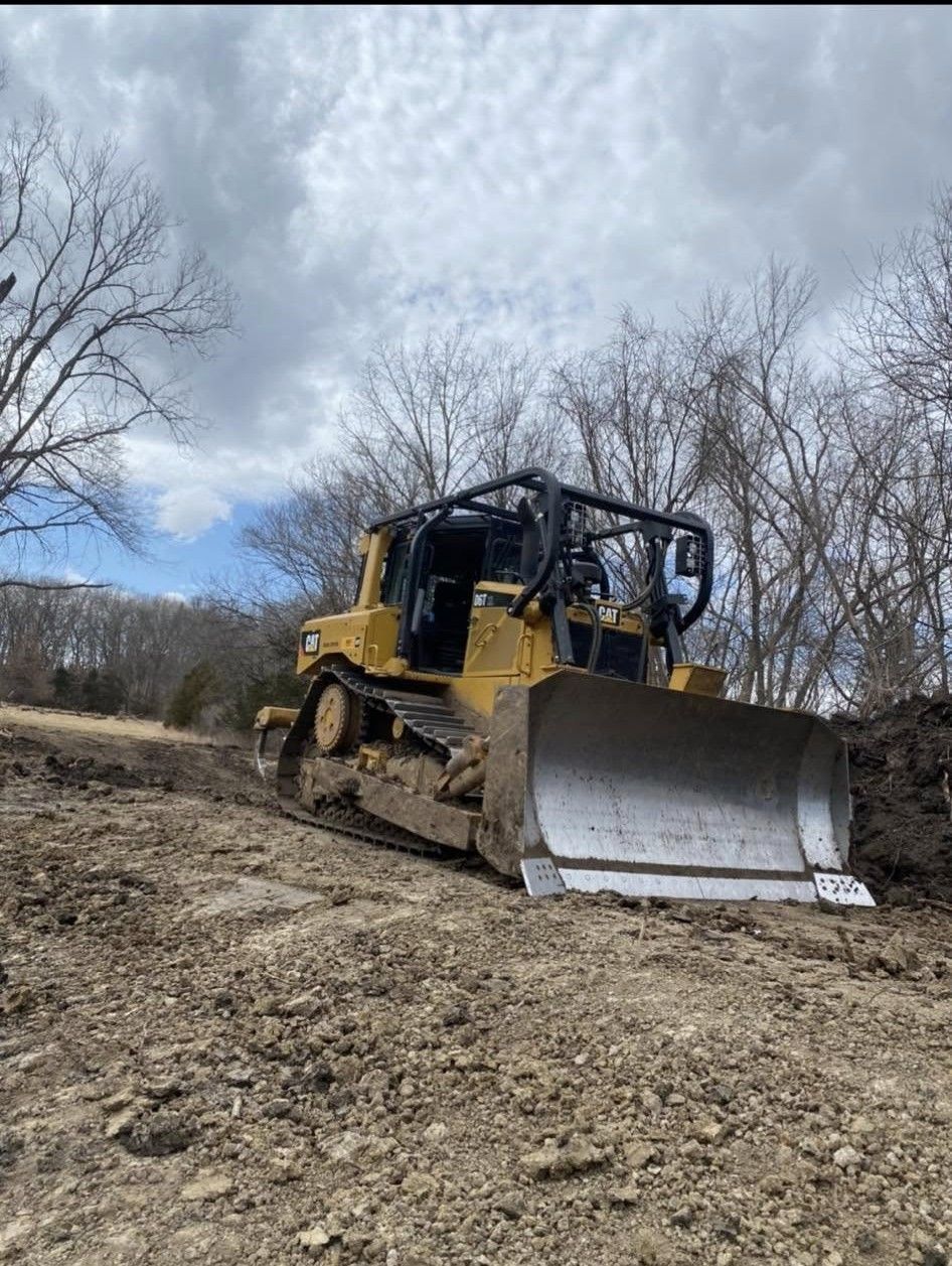 Yellow bulldozer on a dirt slope with bare trees under a cloudy sky