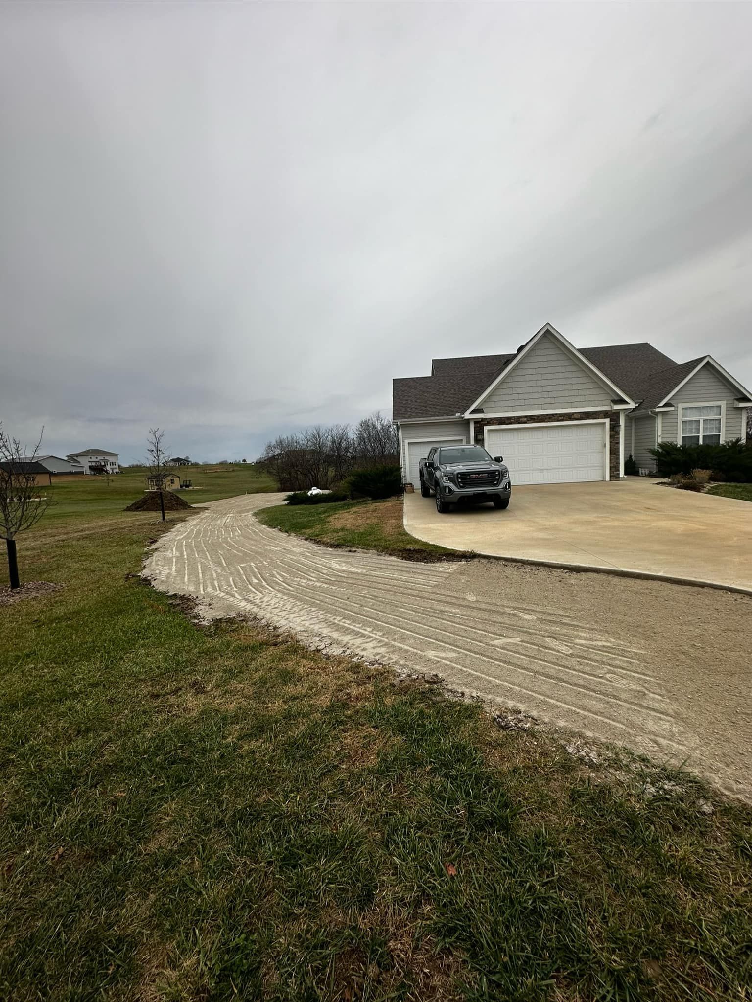 Curving gravel driveway beside a white house with a parked dark SUV under a cloudy sky