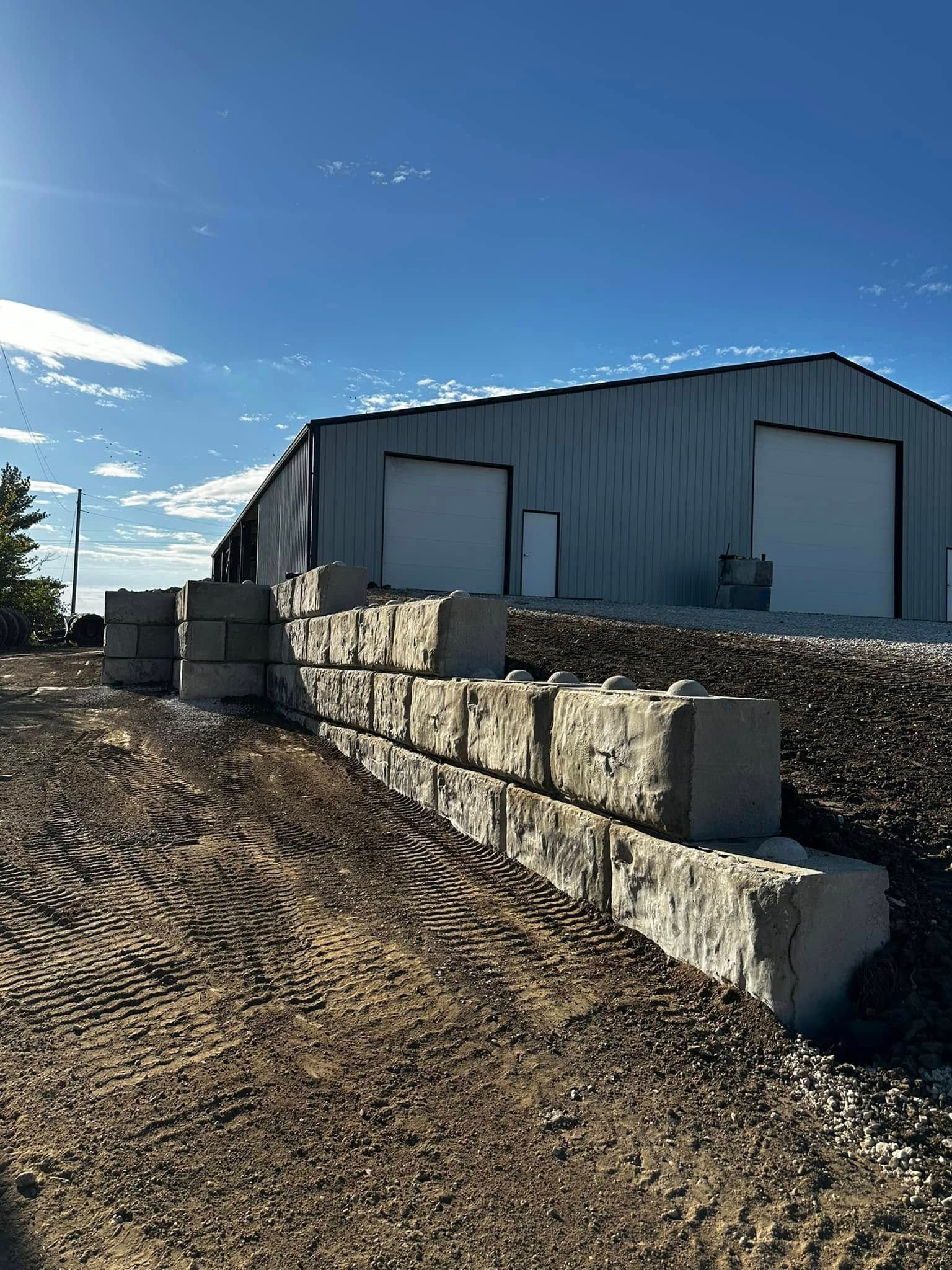 Gravel lot beside a metal warehouse with concrete blocks under a clear blue sky