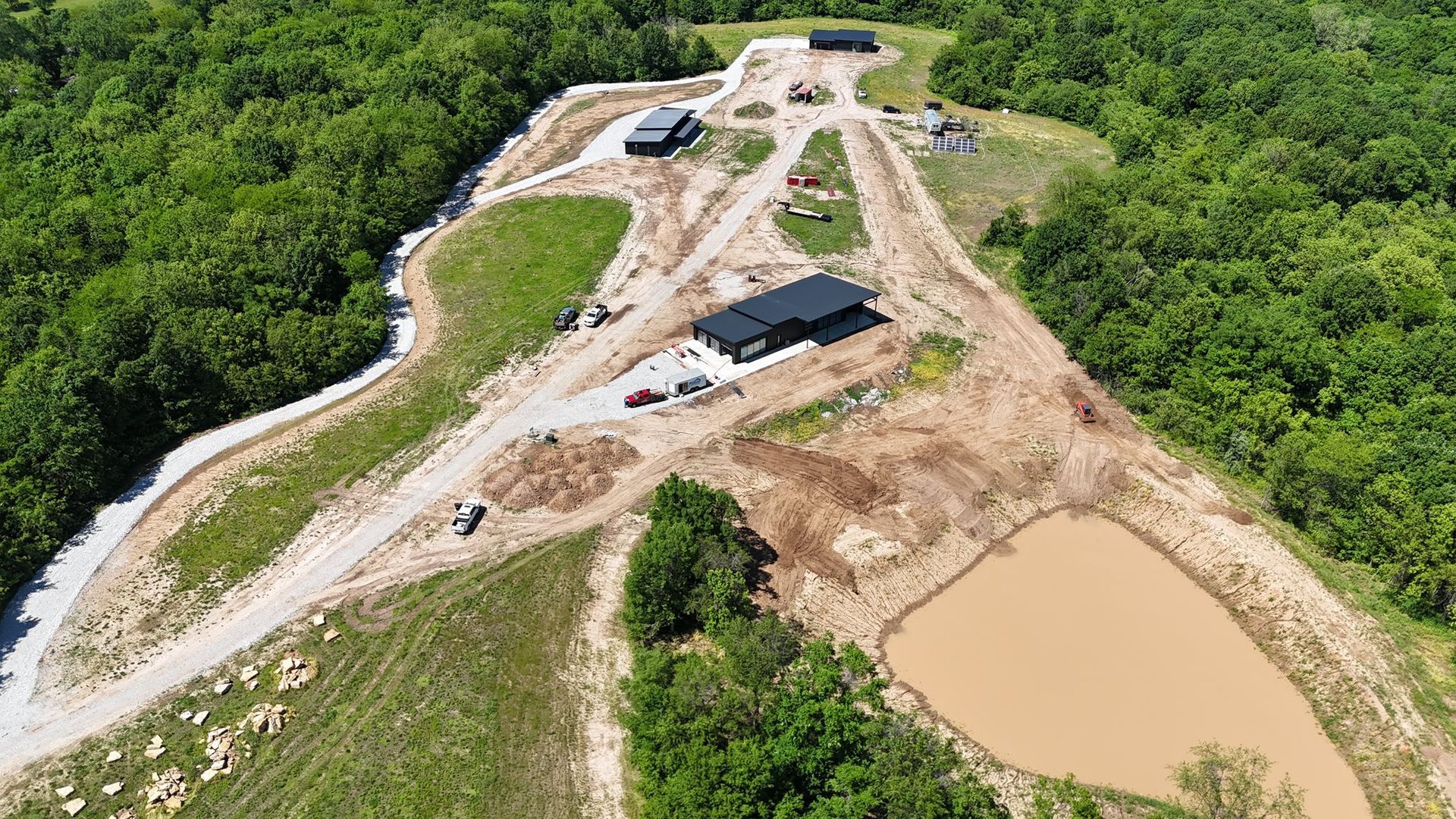 Aerial view of a construction site with dirt roads, excavated earth, and surrounding green forest.