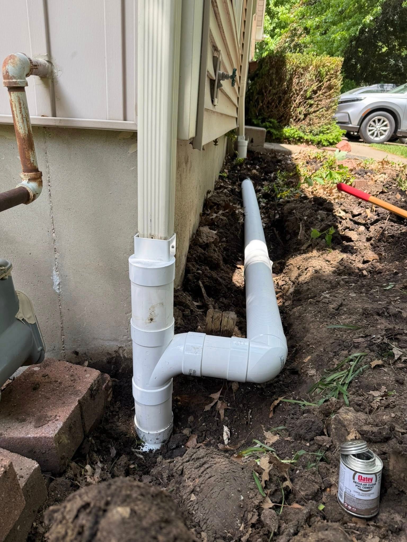 New white PVC drain pipe installed beside a house in a muddy yard.