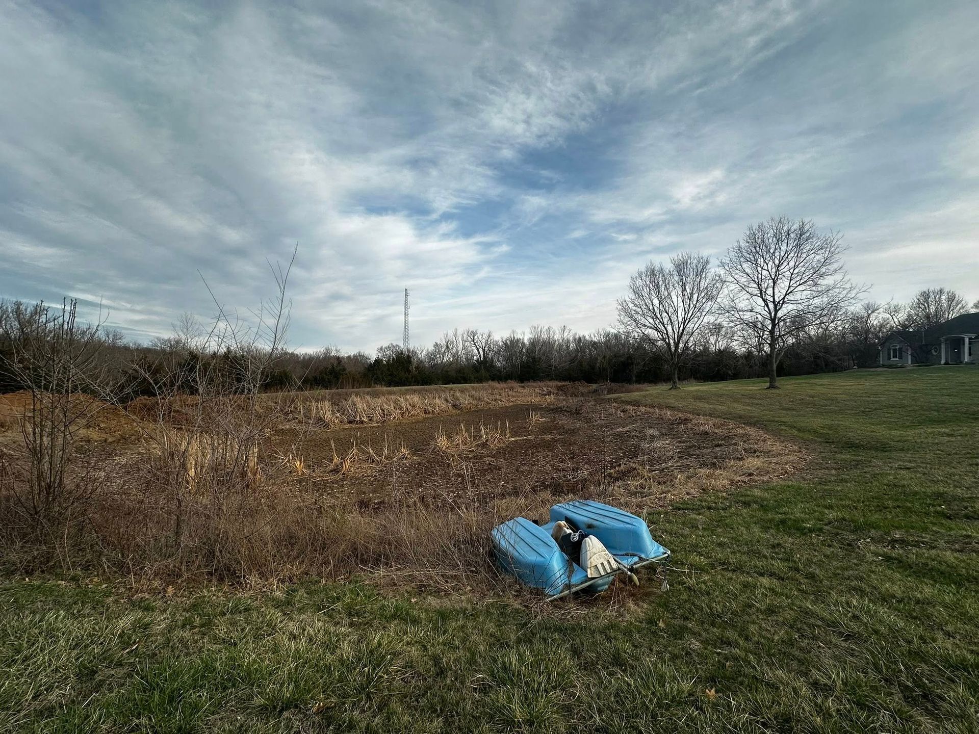 Open field with a blue tarp-covered object in the foreground under a cloudy sky