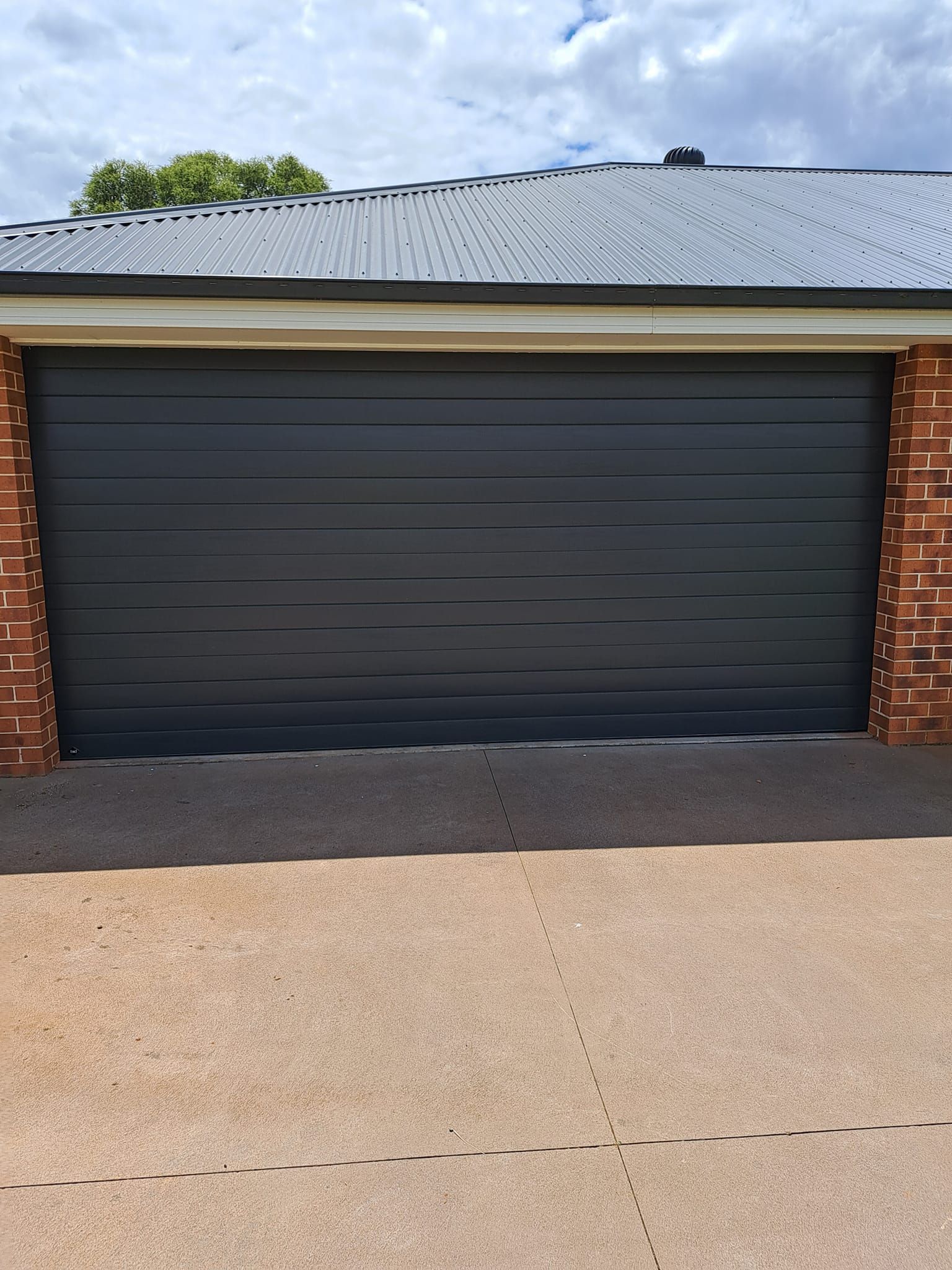 A black electric garage door is sitting in front of a brick building.
