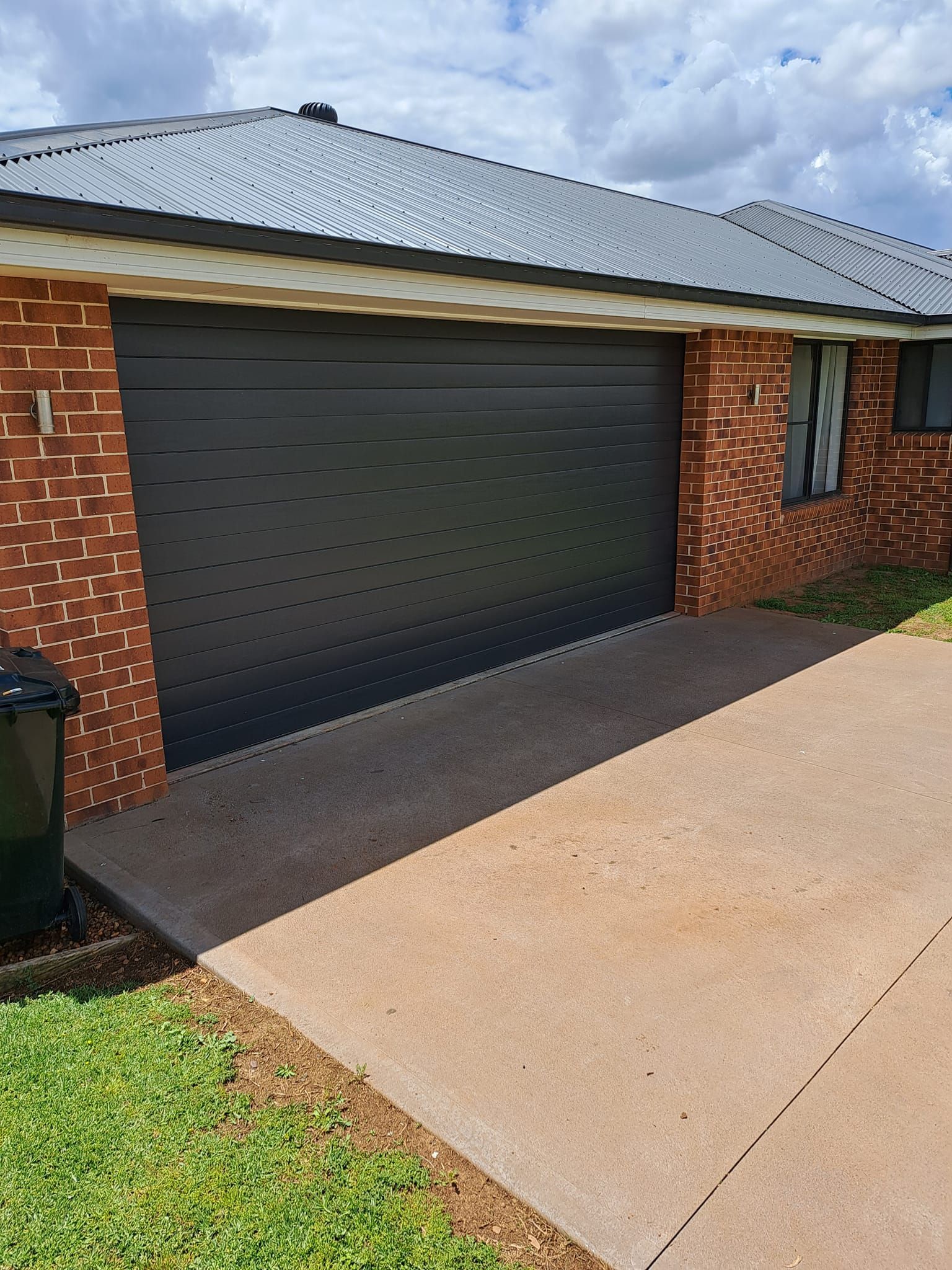 A black roller garage door is sitting in front of a brick house.