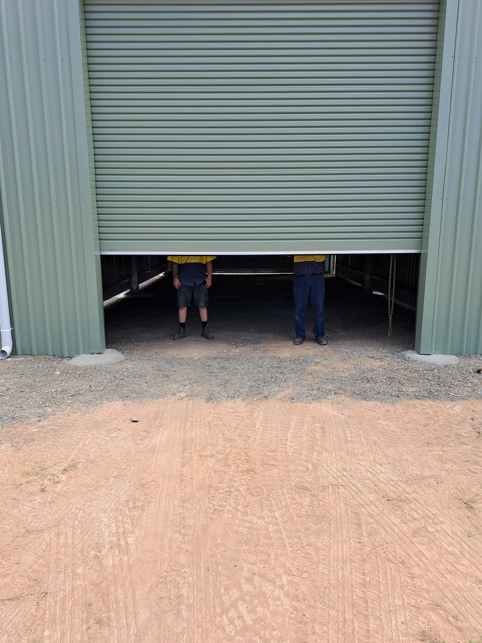 Two men are standing in the doorway of a roller door garage.