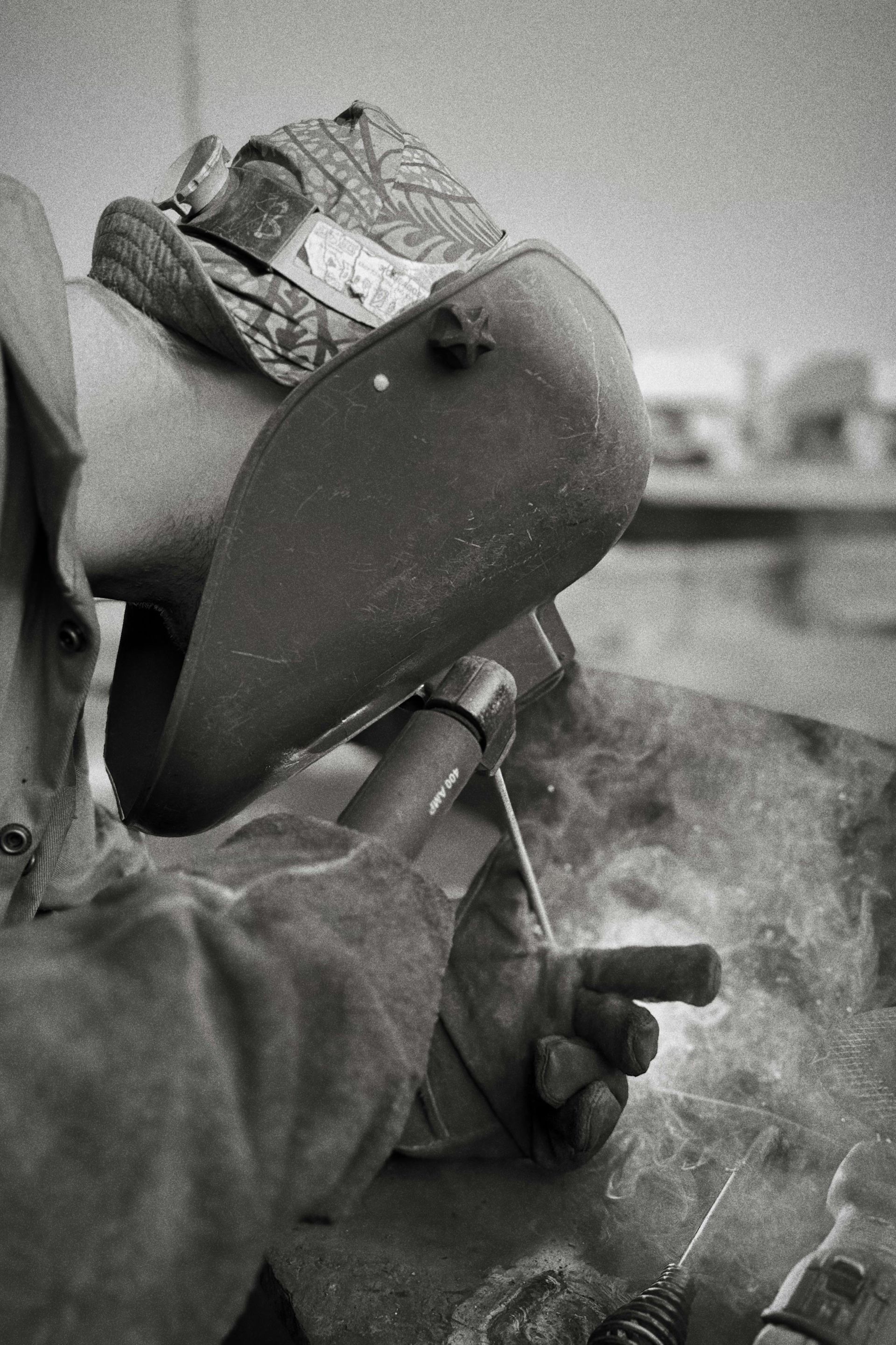 Welder wearing protective gear, welding metal outdoors, creating bright sparks.