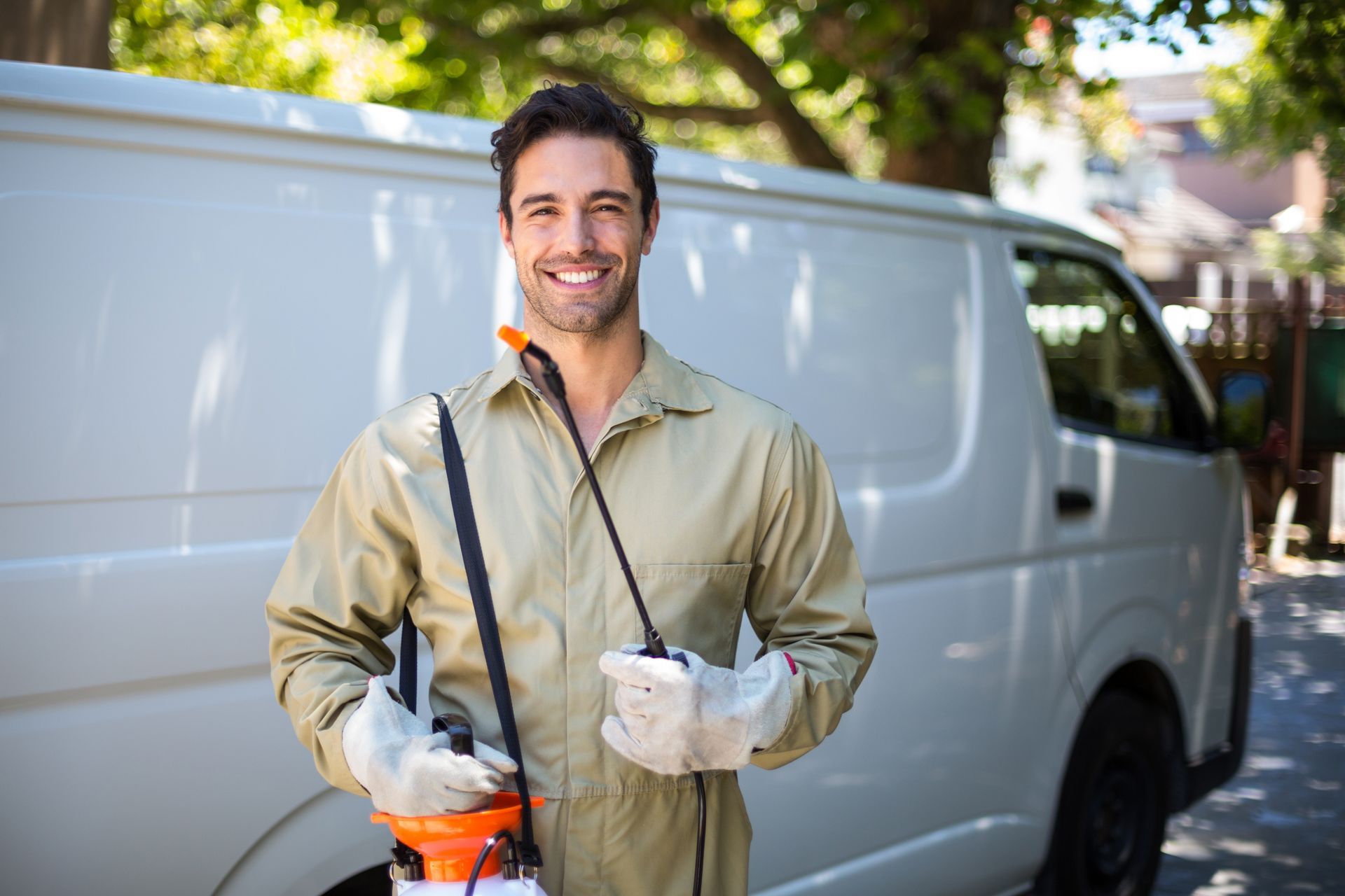 Smiling worker in beige coveralls and white gloves standing beside a white van with tools in hand